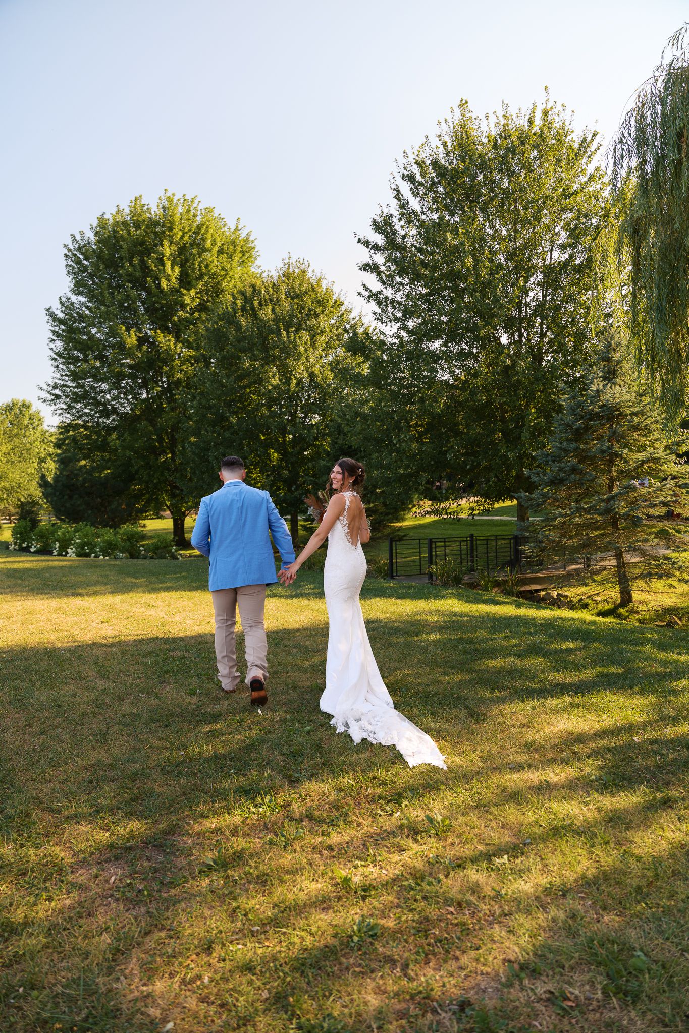 man in blue suit jacket and tan pants holds hands with woman in wedding gown walking away from camera in western pennsylvania