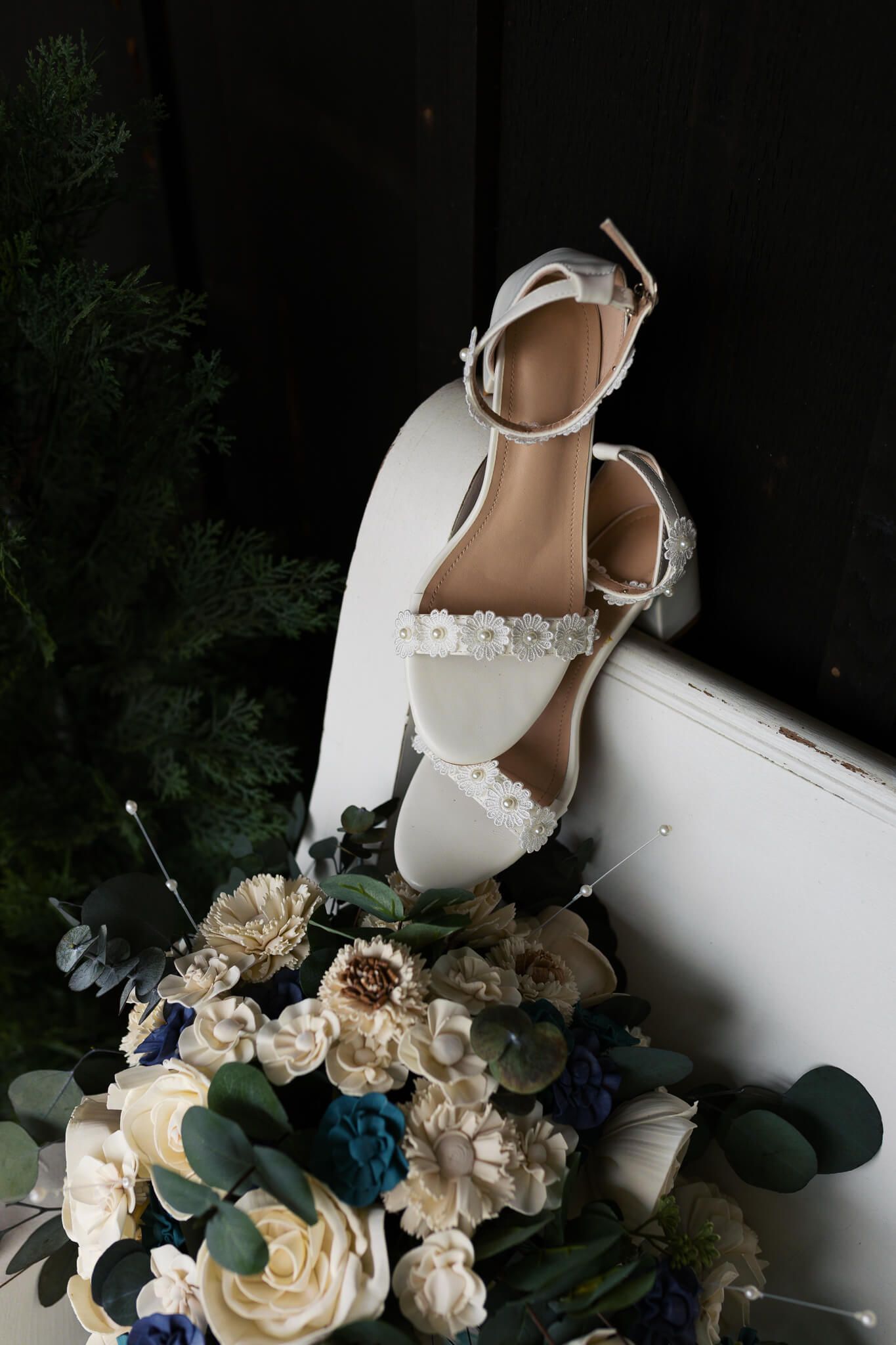 wedding shoes hanging on bench above bouquet of flowers