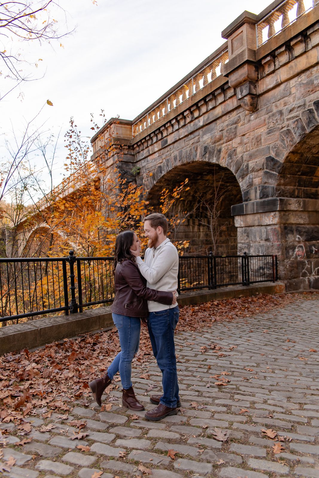 couple dressed in fall attire sharing a kiss in front of a stone bridge in Pittsburgh