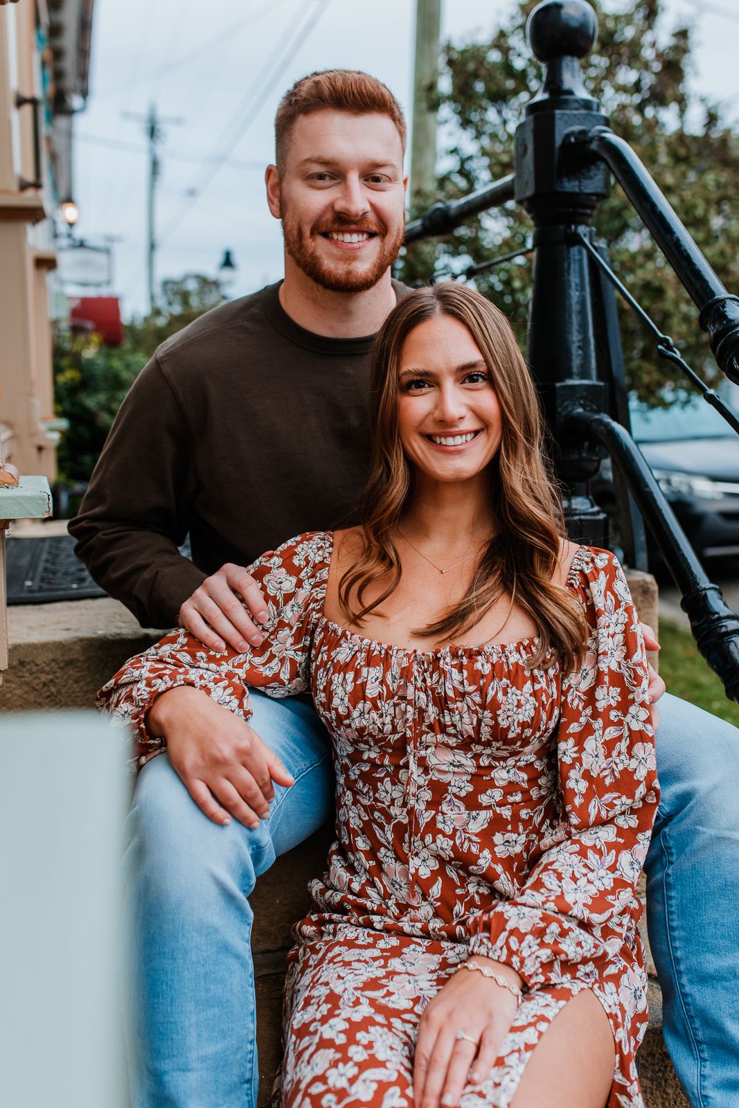 woman sitting in front of man, both smiling at the camera for engagement photos