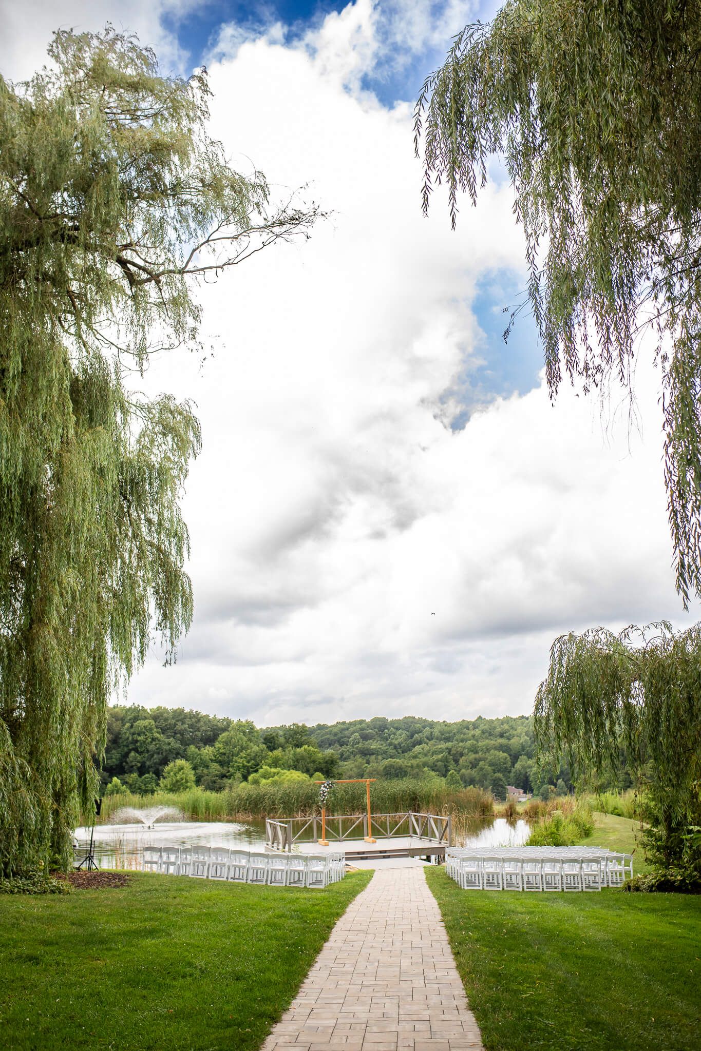 wedding ceremony location view of dock on lake surrounded by white chairs and willow trees