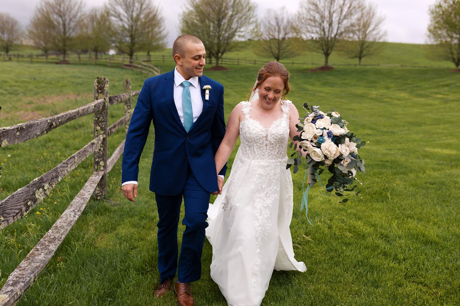 man and woman walking along fence line laughing while bride carries her wedding bouquet