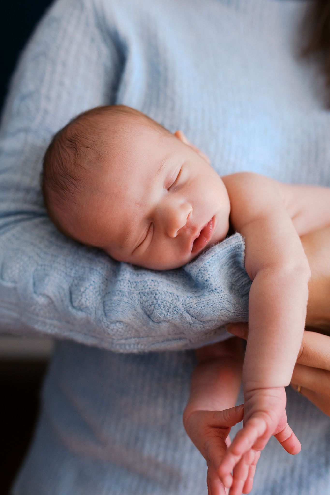 photo of a beautiful baby boy with clear skin laying in the arms of his mom while sleeping