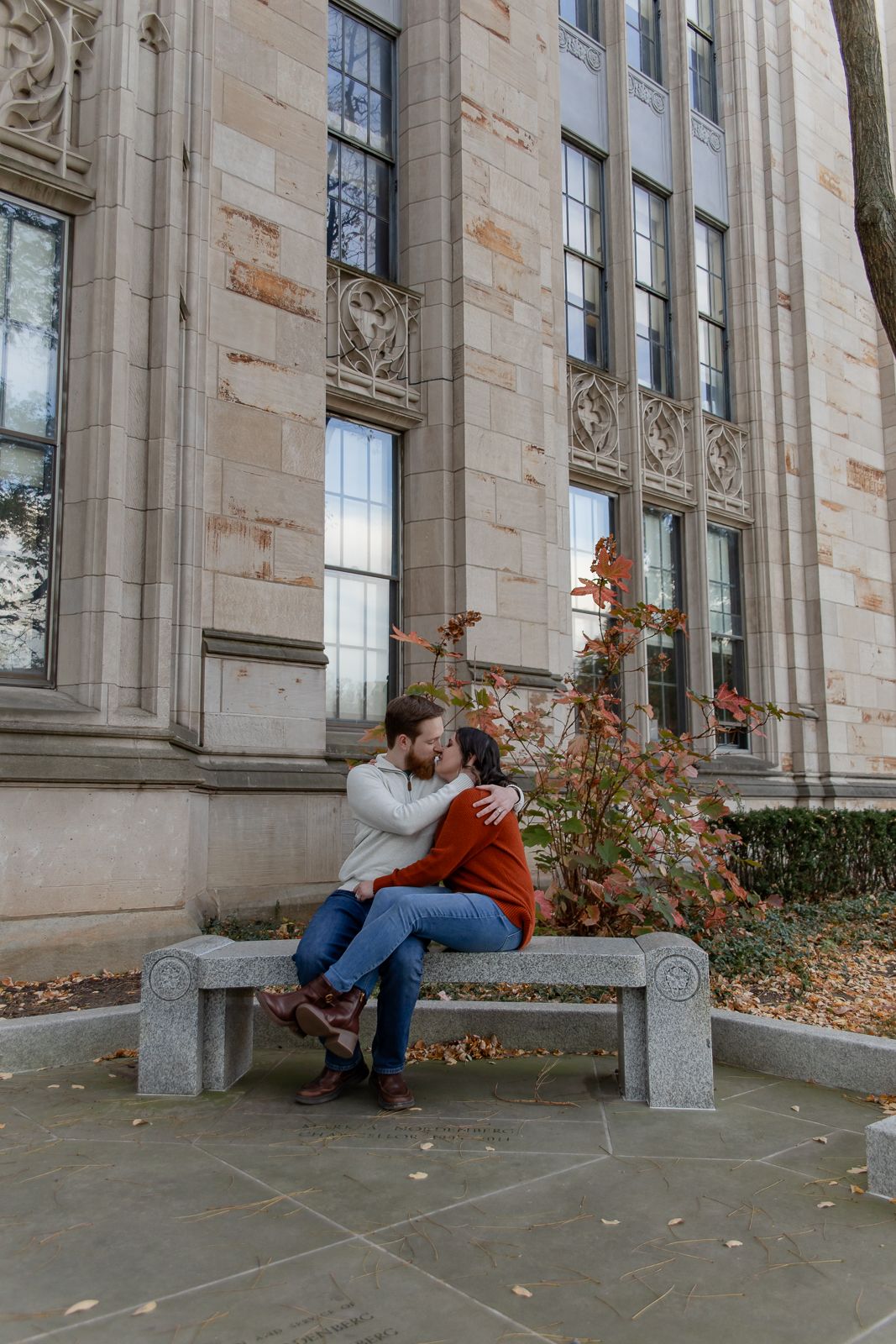 couple sitting on bench at University of Pittsburgh sharing a kiss during their engagement session