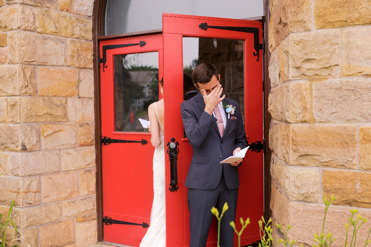groom becoming emotional while reading his private vows behind a red door to his bride