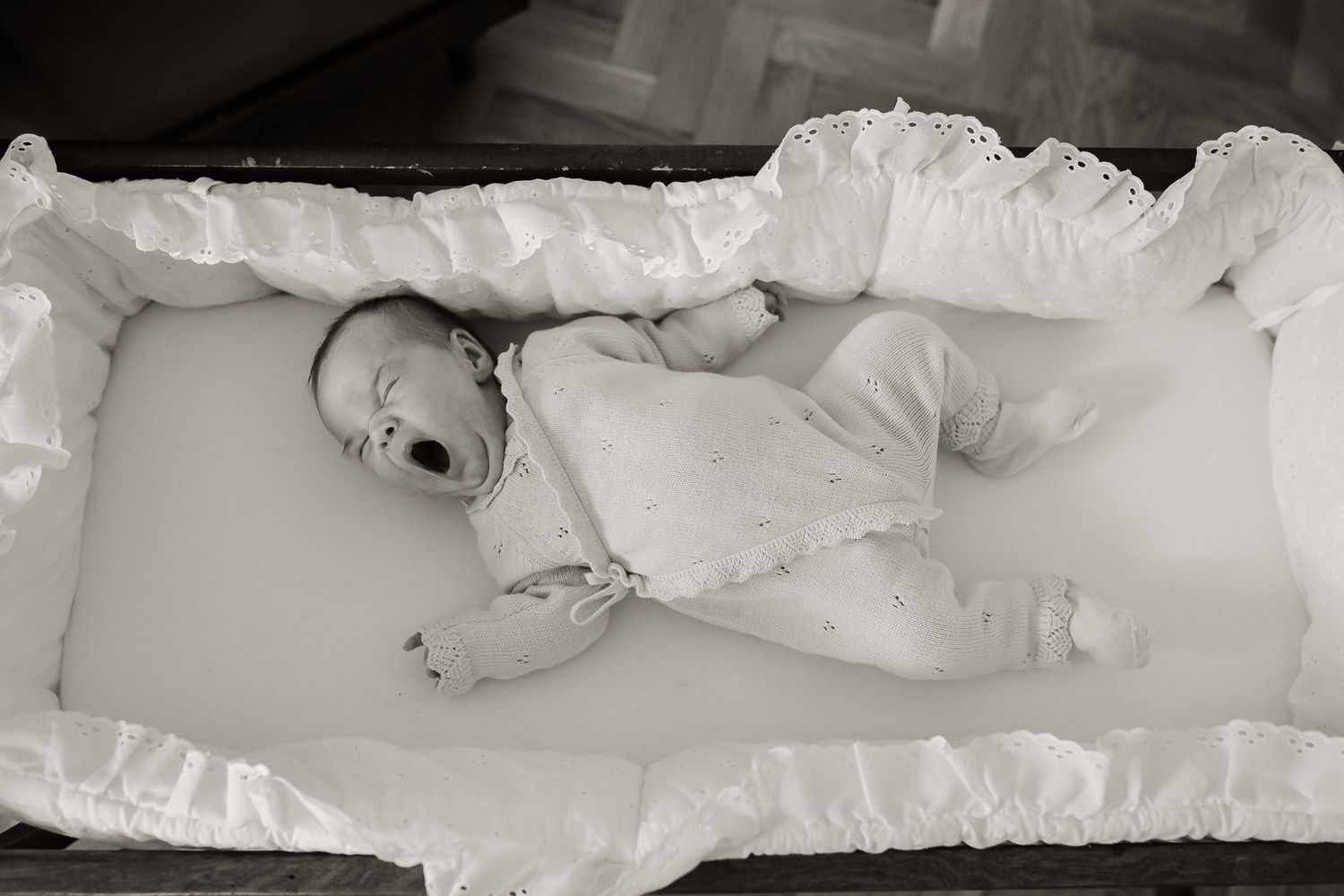 baby yawning in crib in a black and white photo during an in-home newborn session