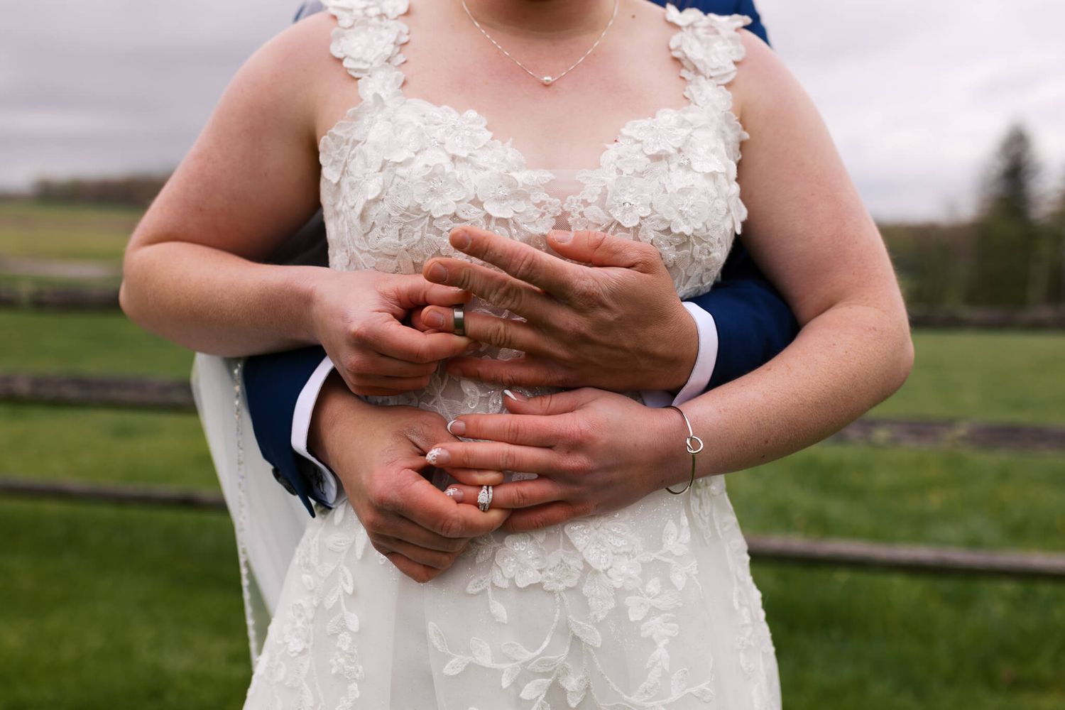 hands of bride and groom wrapped around womans waist while putting each others wedding rings on