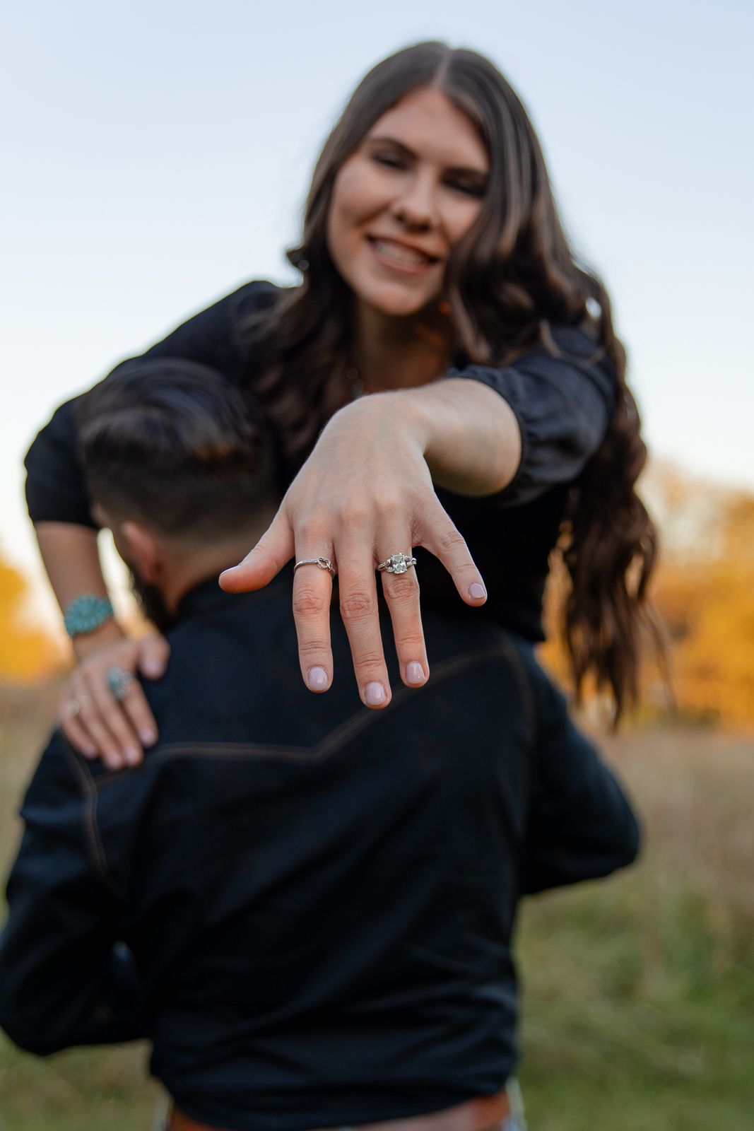 smiling woman showing off her engagement ring over her fiances shoulder