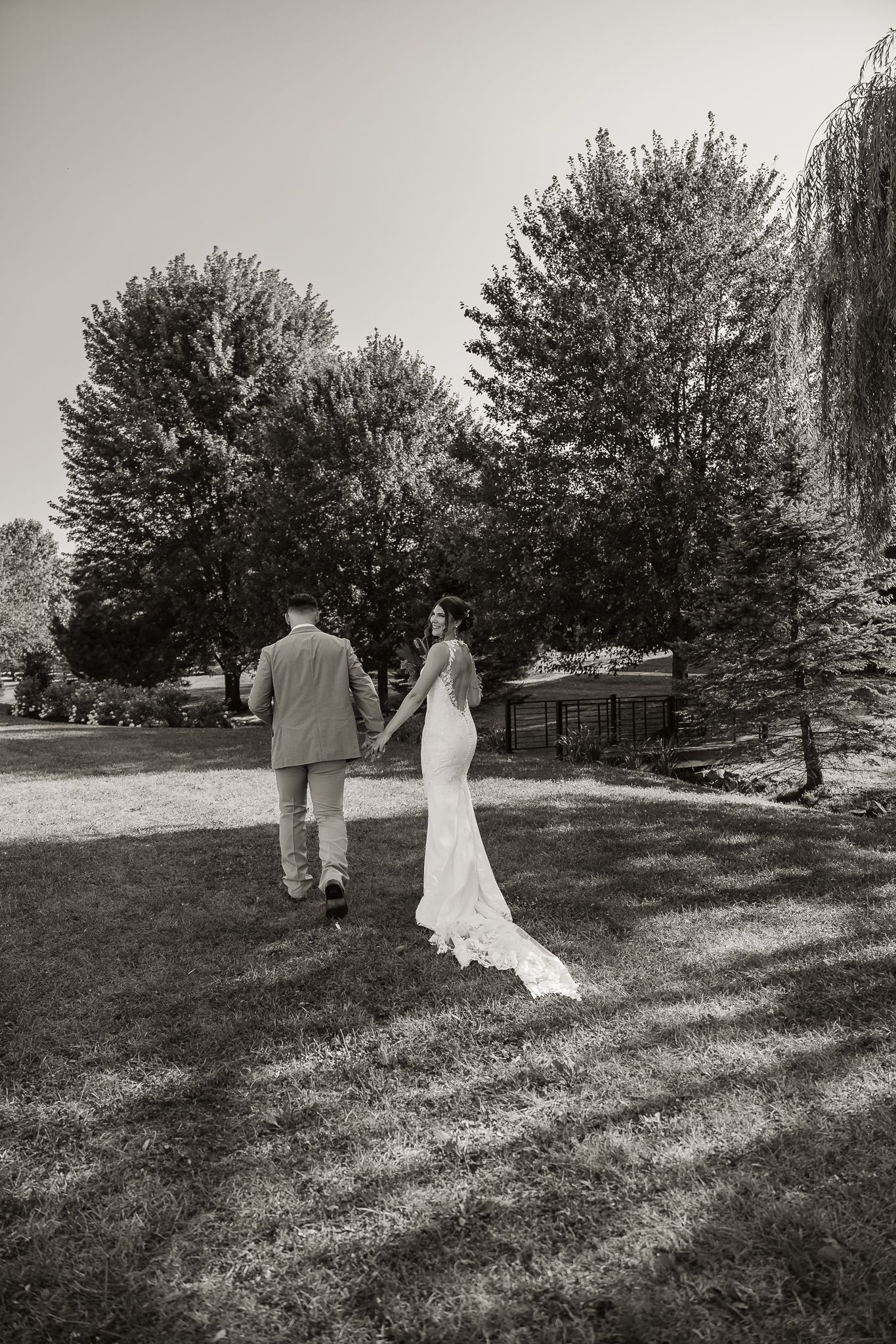 black and white image of bride and groom holding hands while she looks over her left shoulder while walking away from the camera