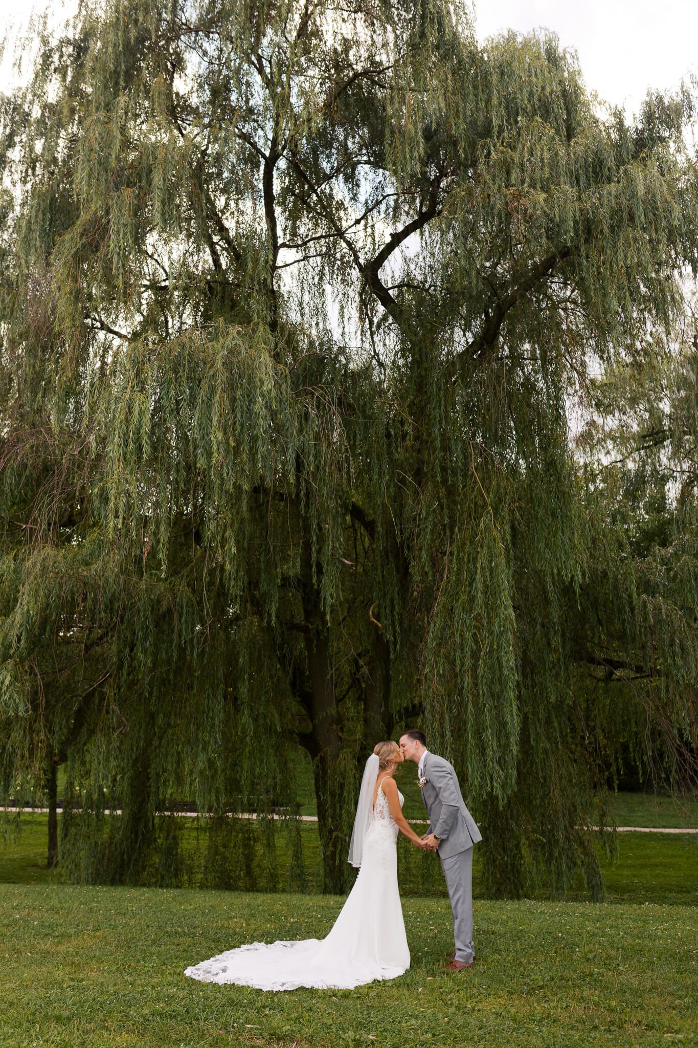 Couple shares a kiss under willow tree at picturesque wedding venue in Western Pennsylvania