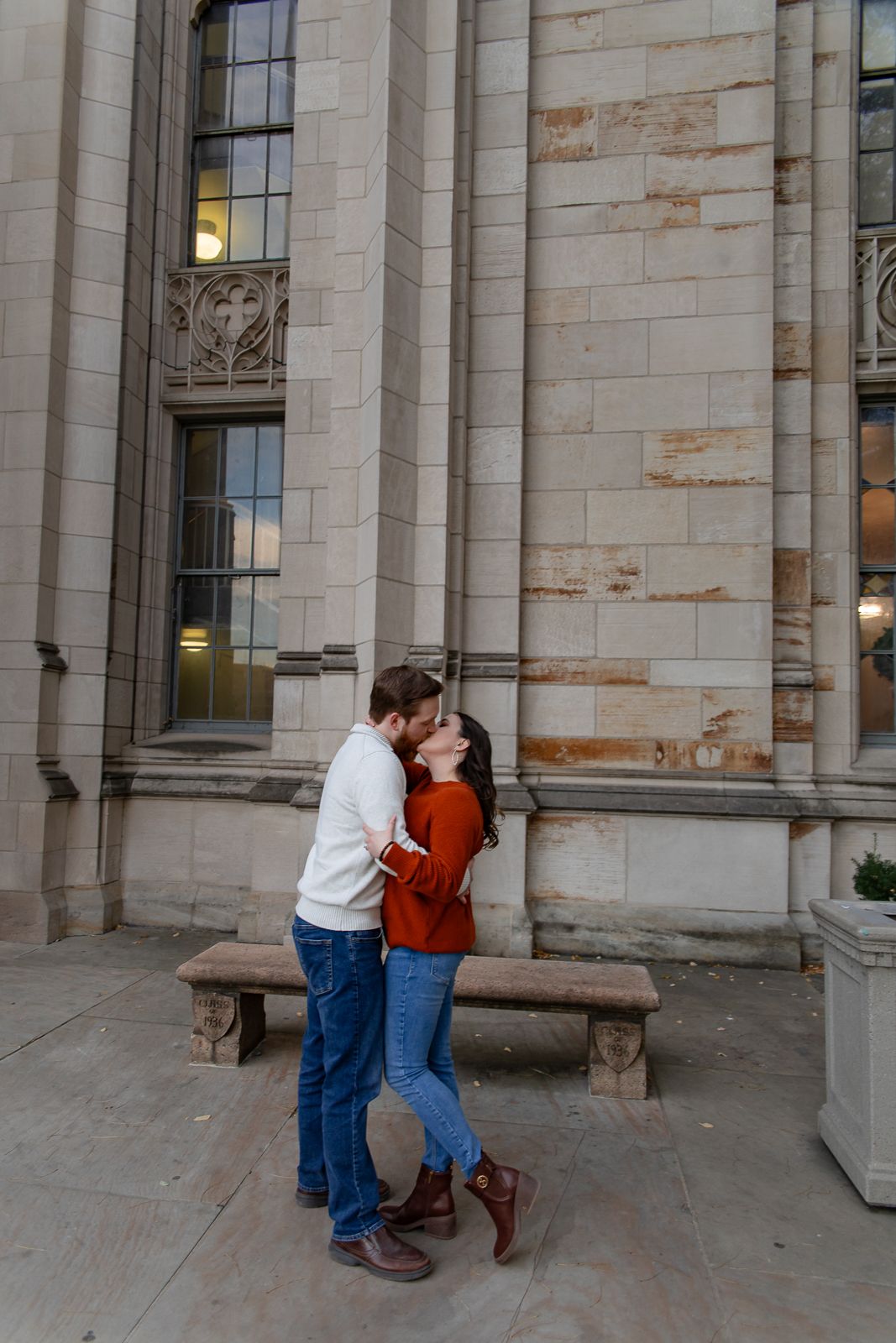 man in white sweater and blue jeans kisses woman in red sweater and blue jeans