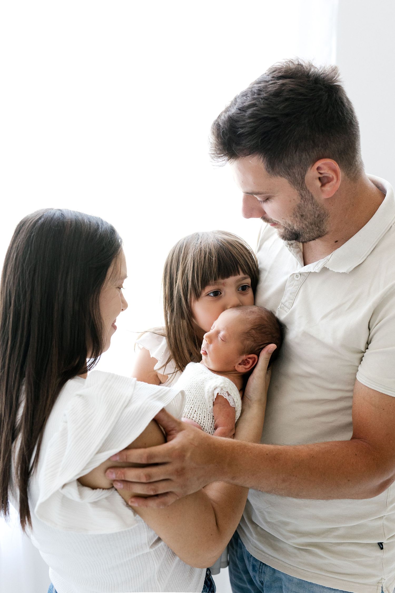 Happy family of four with father holding newborn baby while mother and young daughter look on lovingly.