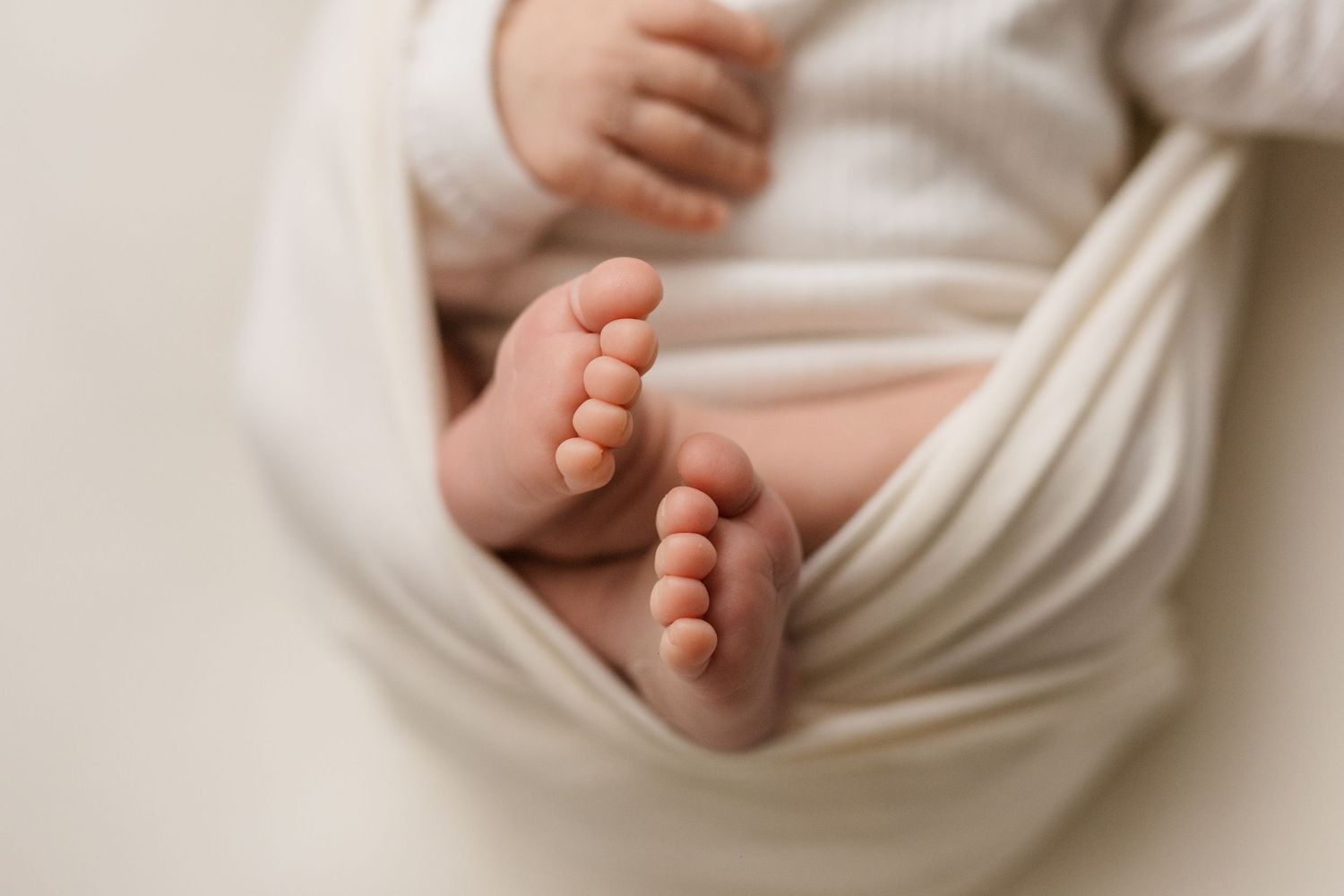 Close-up of tiny newborn baby feet peeking out from a soft white swaddle wrap.