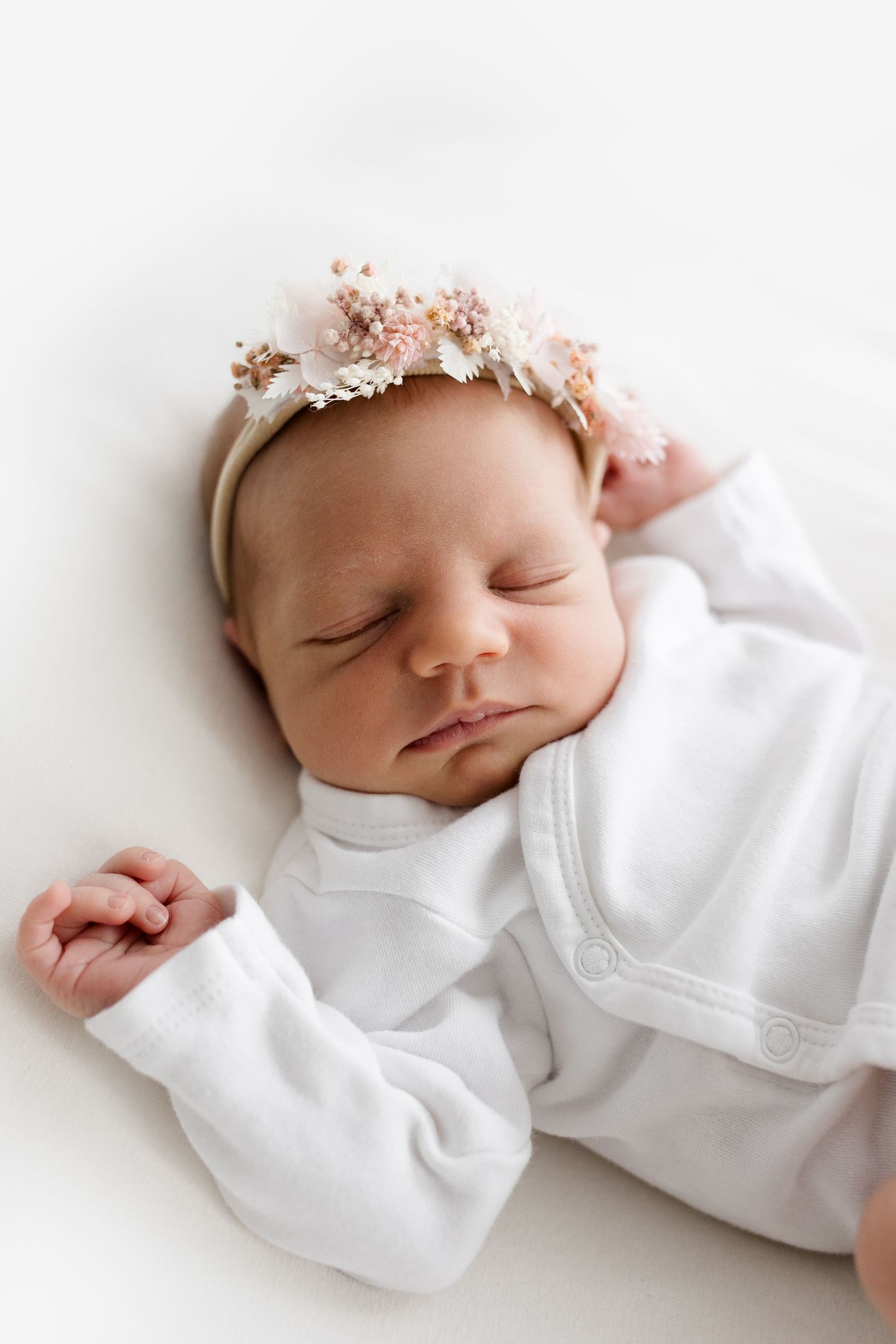 Sleeping newborn baby girl in white outfit wearing a delicate floral headband.