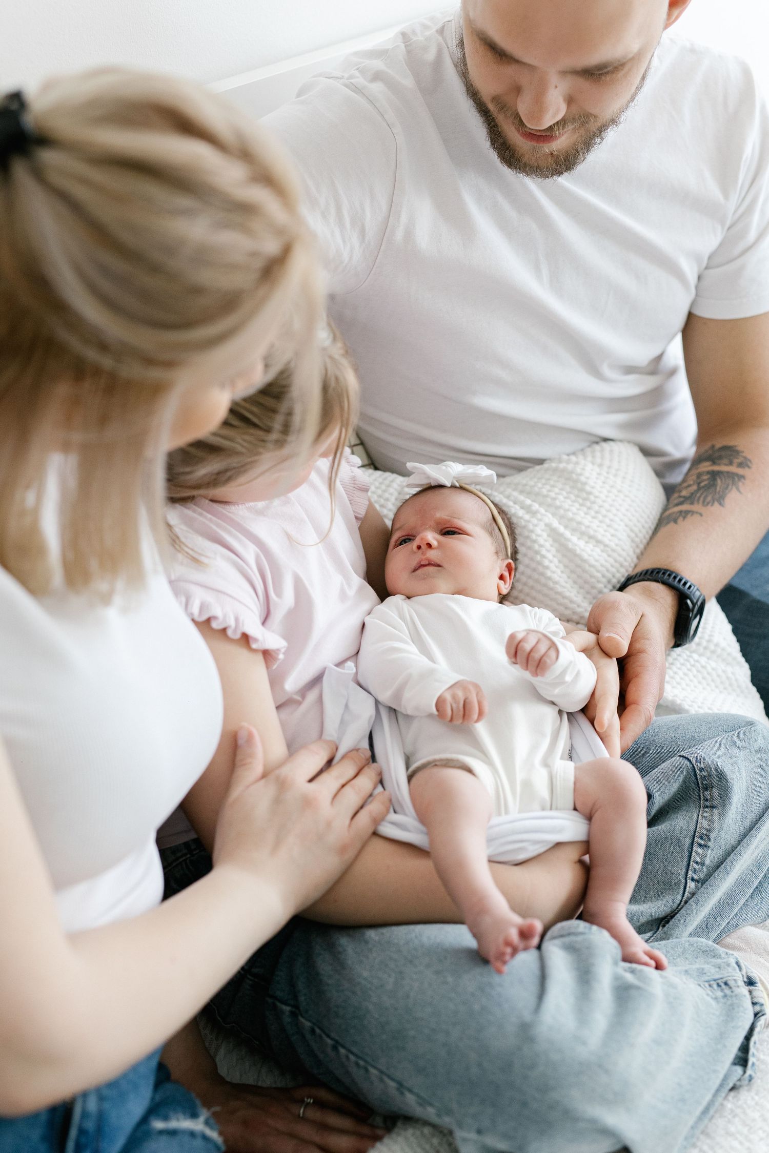 Parents and young daughter admiring newborn baby lying on fathers lap at home.