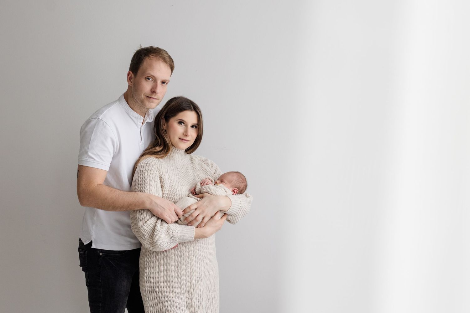 Happy young family with father and mother holding newborn baby in knit outfit.