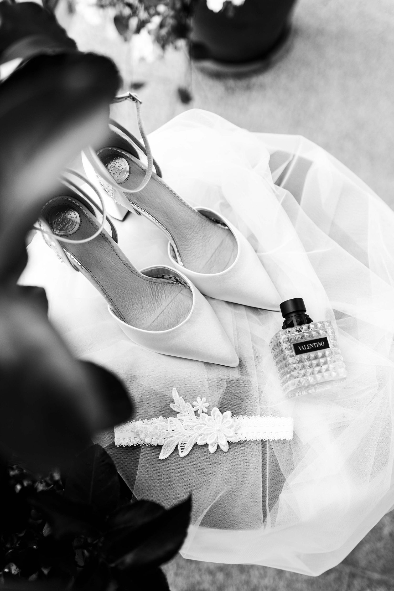Črno-beli poročni flat lay: čevlji, tančica, podvezica in parfum Valentino.