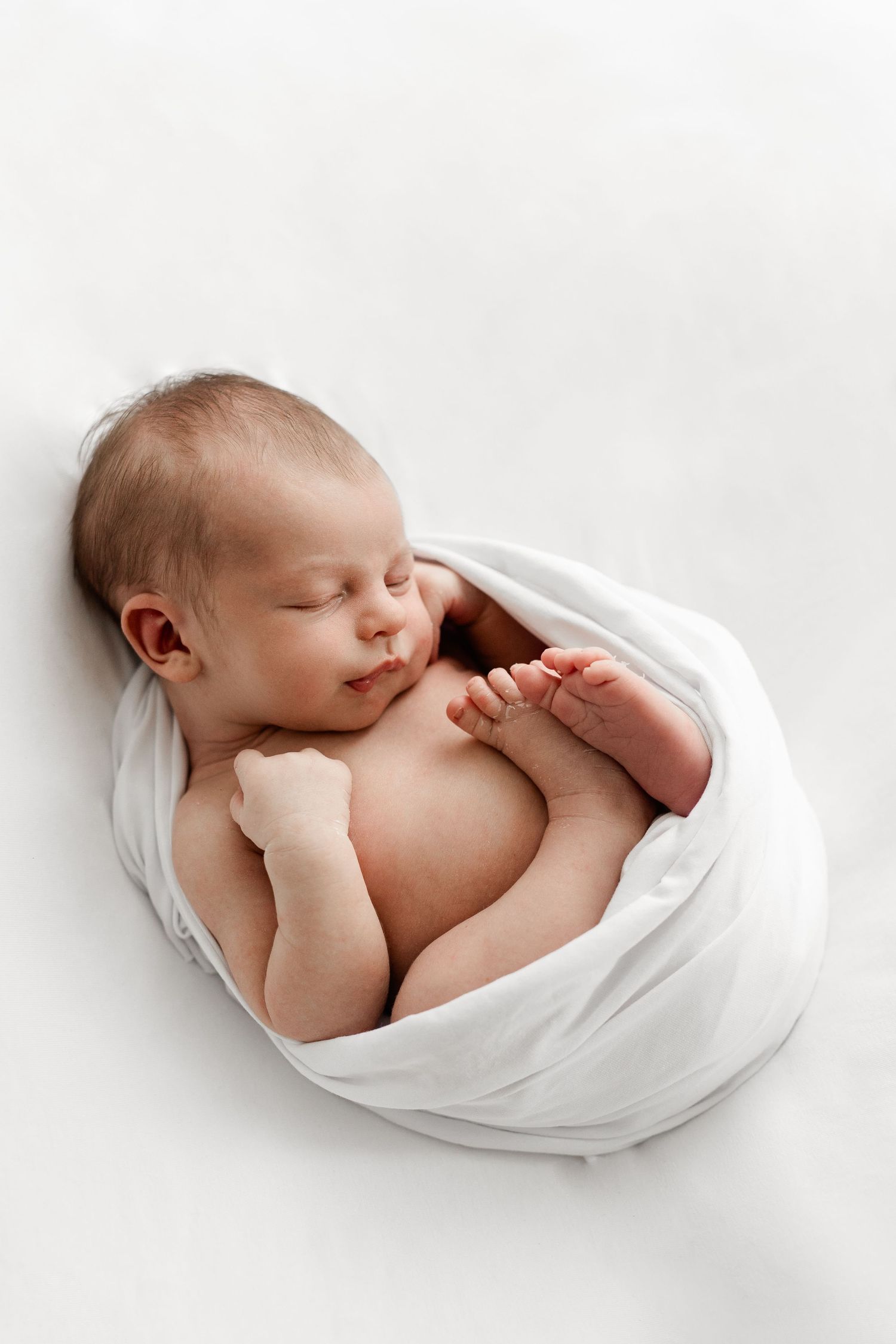 Peaceful sleeping newborn baby wrapped in a soft white swaddle on a white background.