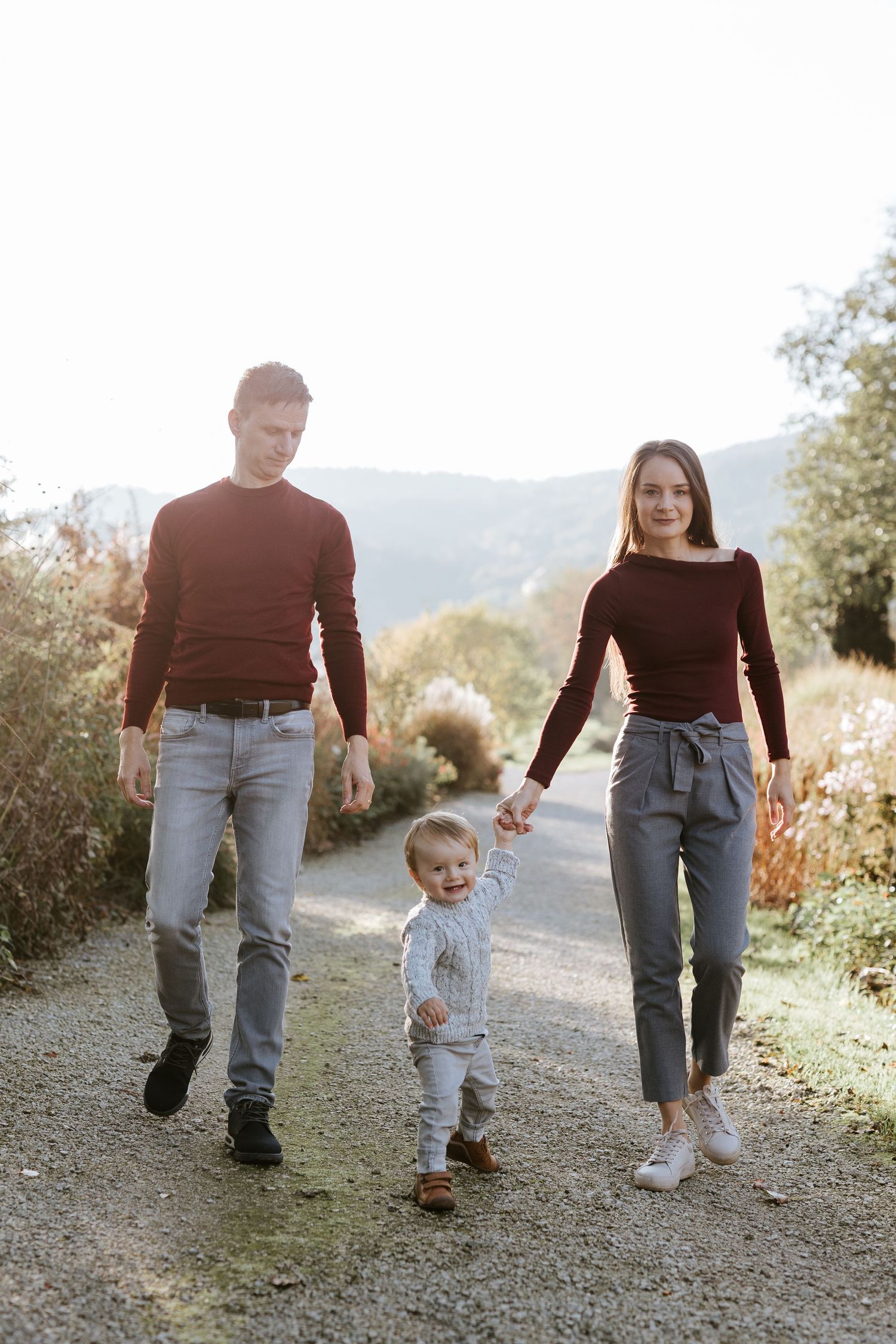 Young family with toddler walking hand in hand on a scenic autumn countryside path.