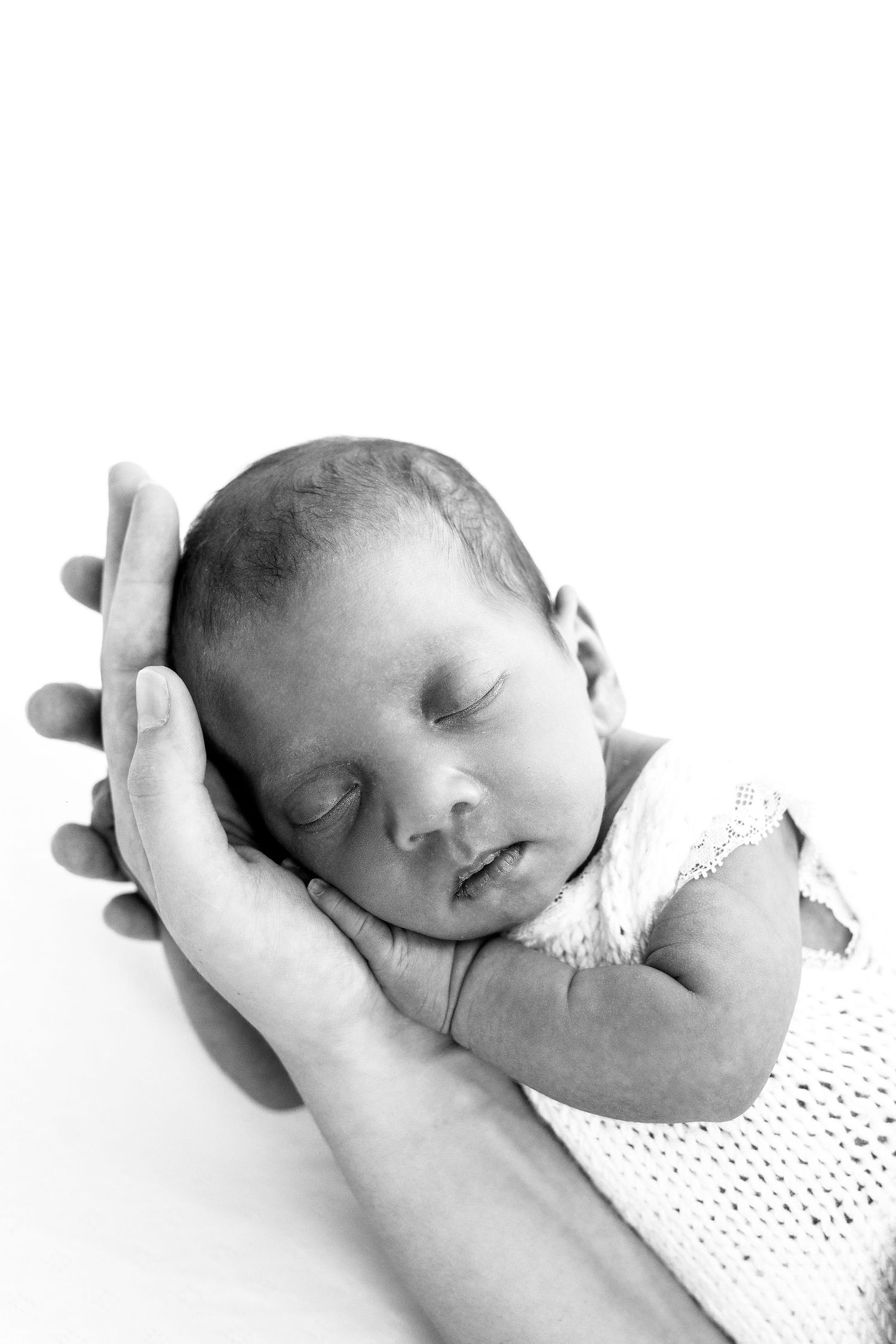 A black and white photo of a sleeping newborn baby cradled gently in a parents hands.