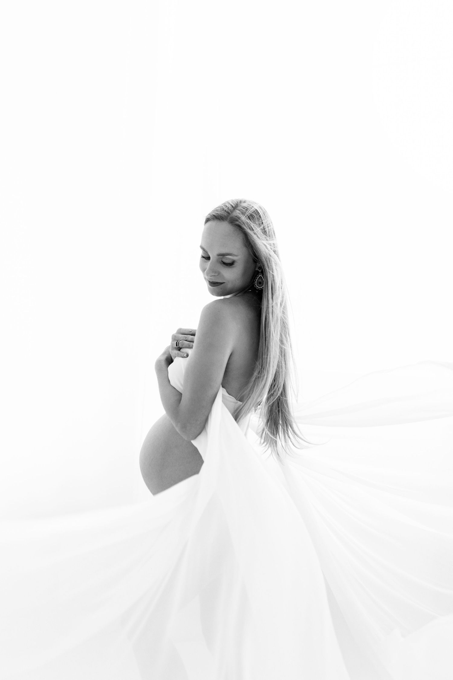 Black and white maternity photo of pregnant woman in flowing white dress.