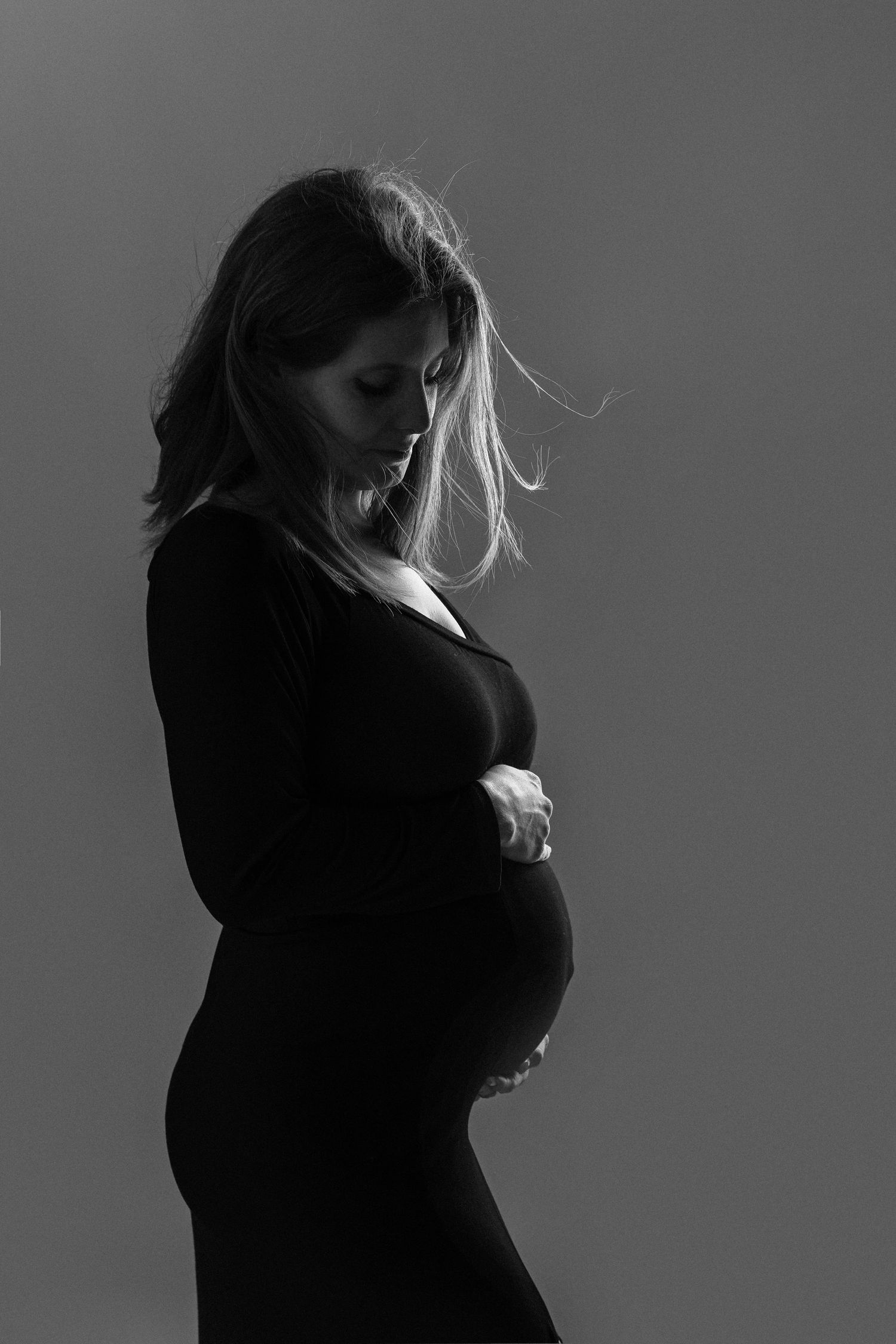 Black and white silhouette portrait of a pregnant woman in black dress holding her belly.