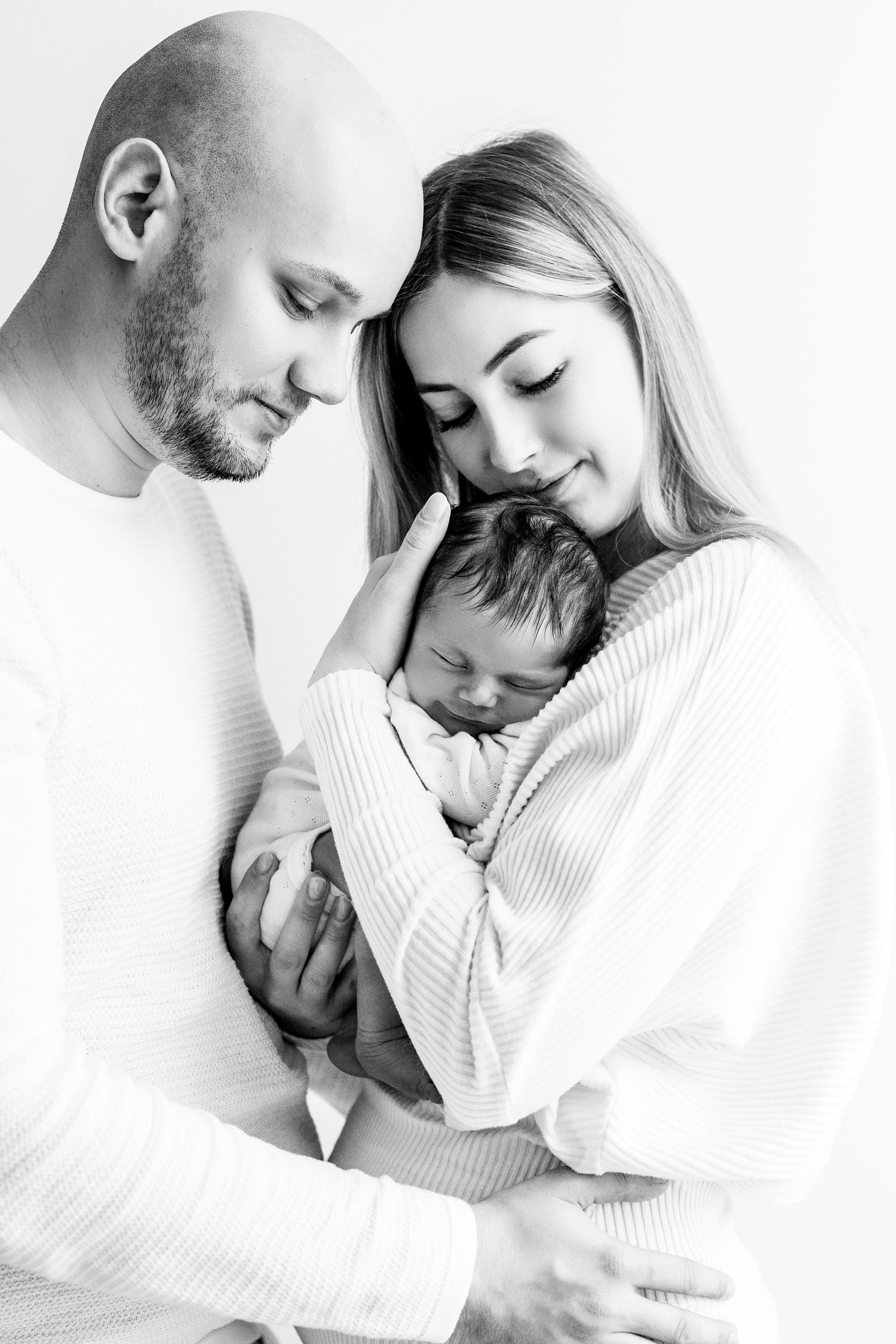 Black and white portrait of parents tenderly holding sleeping newborn baby together.