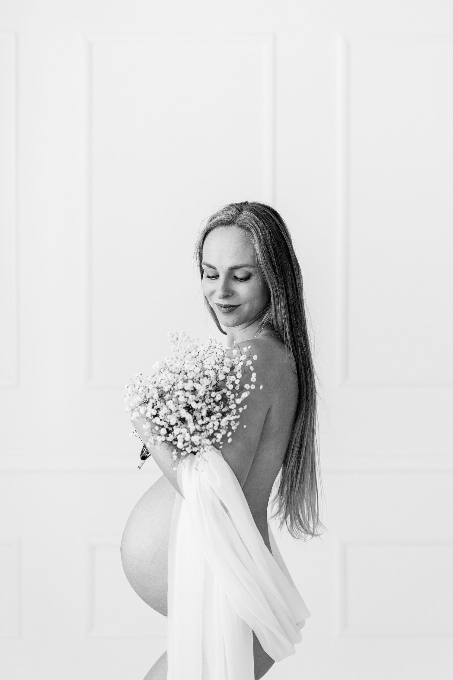 Black and white maternity portrait of woman holding white flowers in studio.