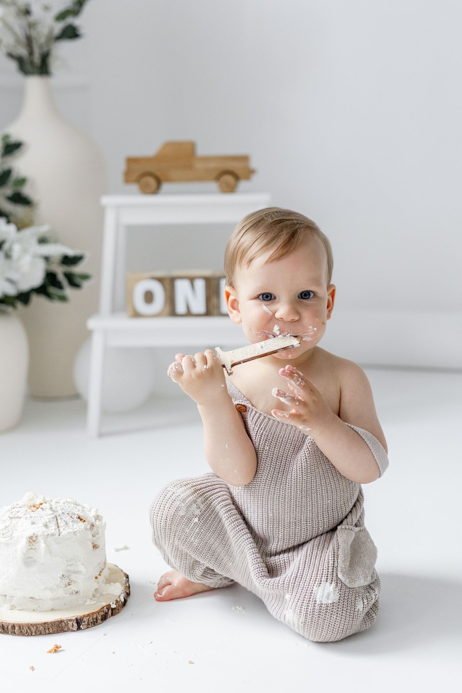 Baby boy in knit outfit eating cake during first birthday cake smash session.