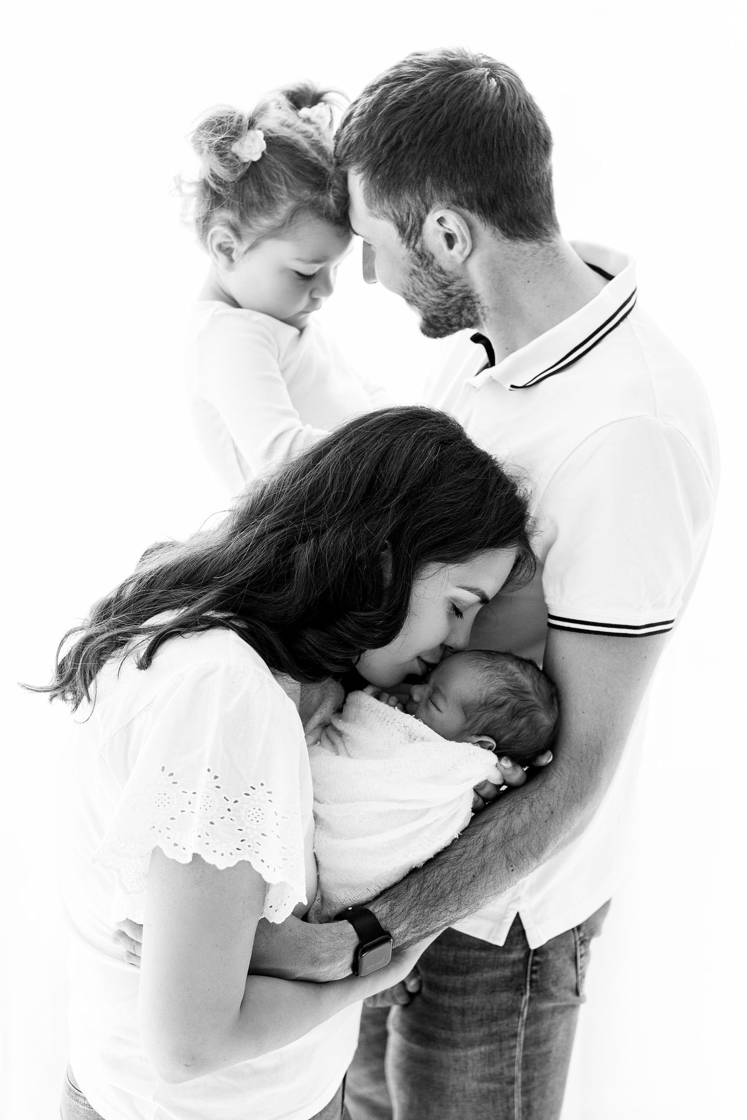 Black and white family portrait with parents and toddler lovingly holding newborn baby.