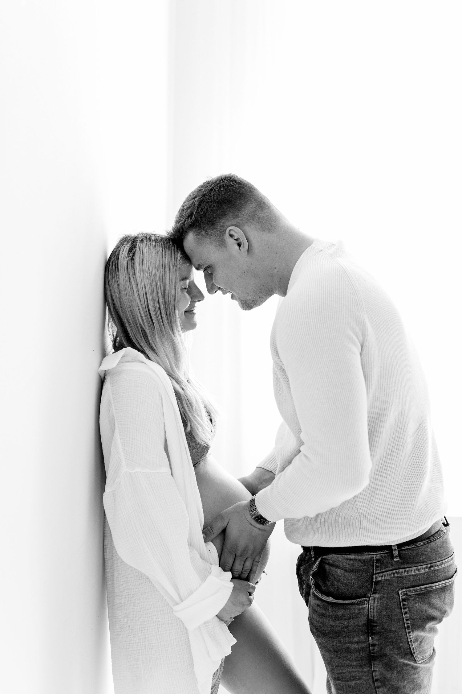 Black and white photo of expecting couple touching foreheads while holding pregnant belly.