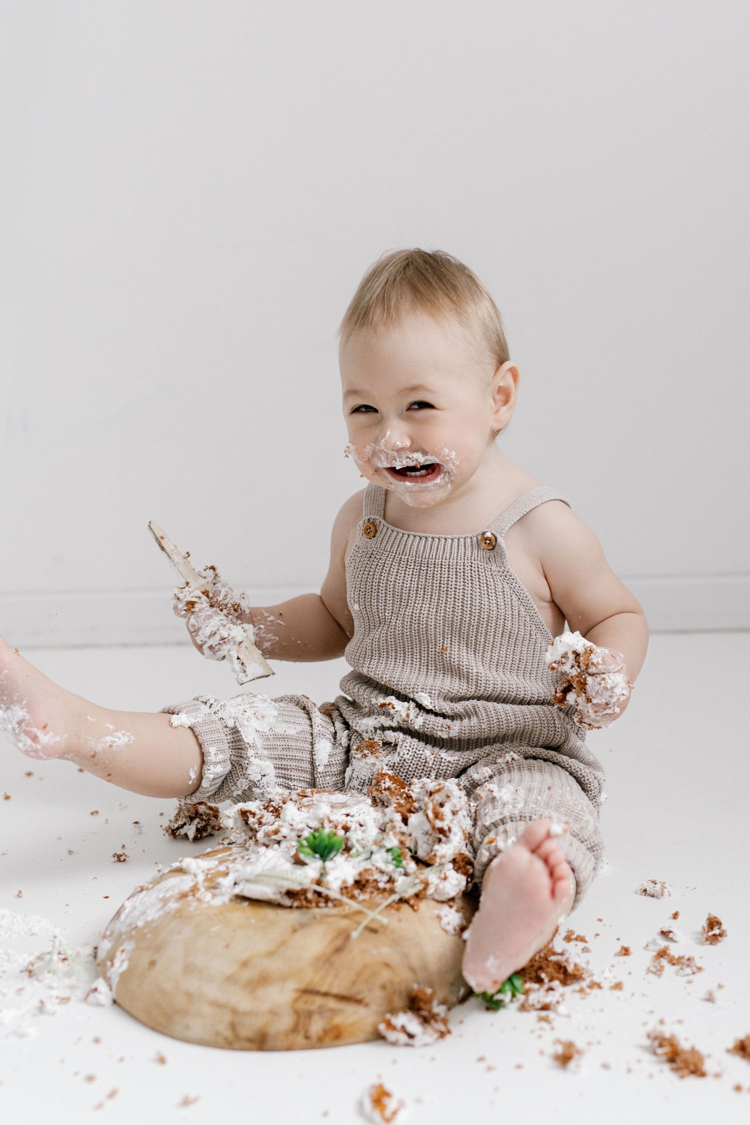 Laughing baby covered in frosting during first birthday cake smash in knit romper.