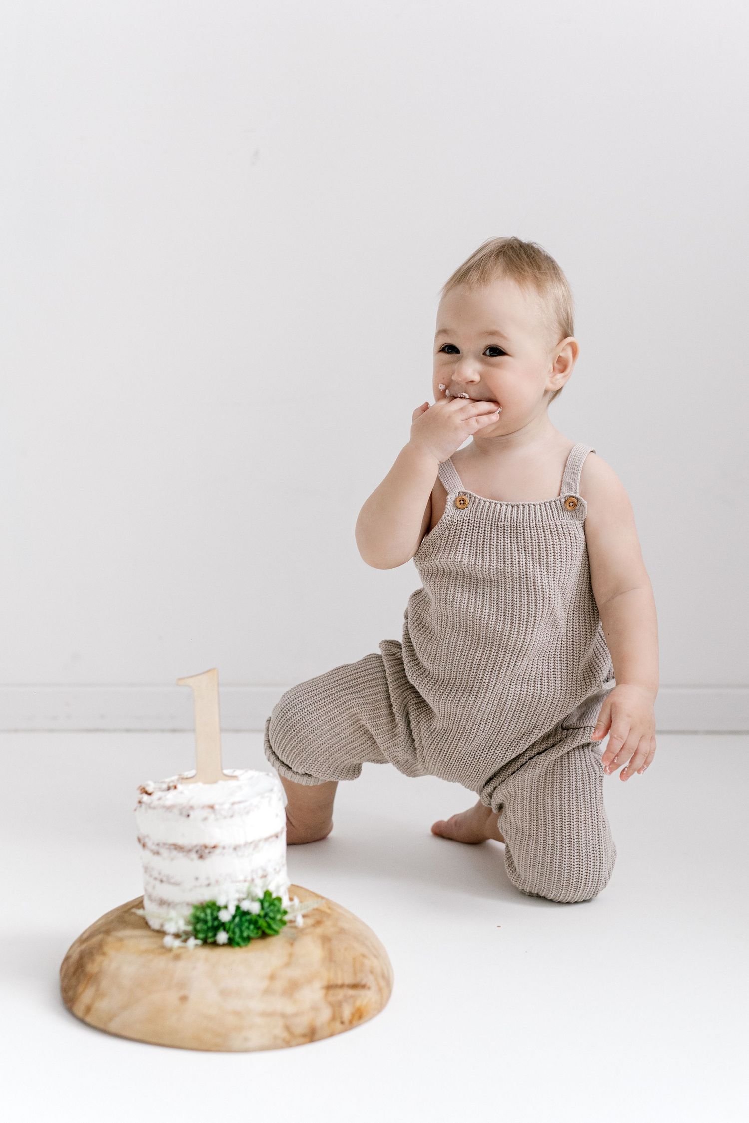 Happy one year old baby in striped romper eating first birthday cake smash on wood board.