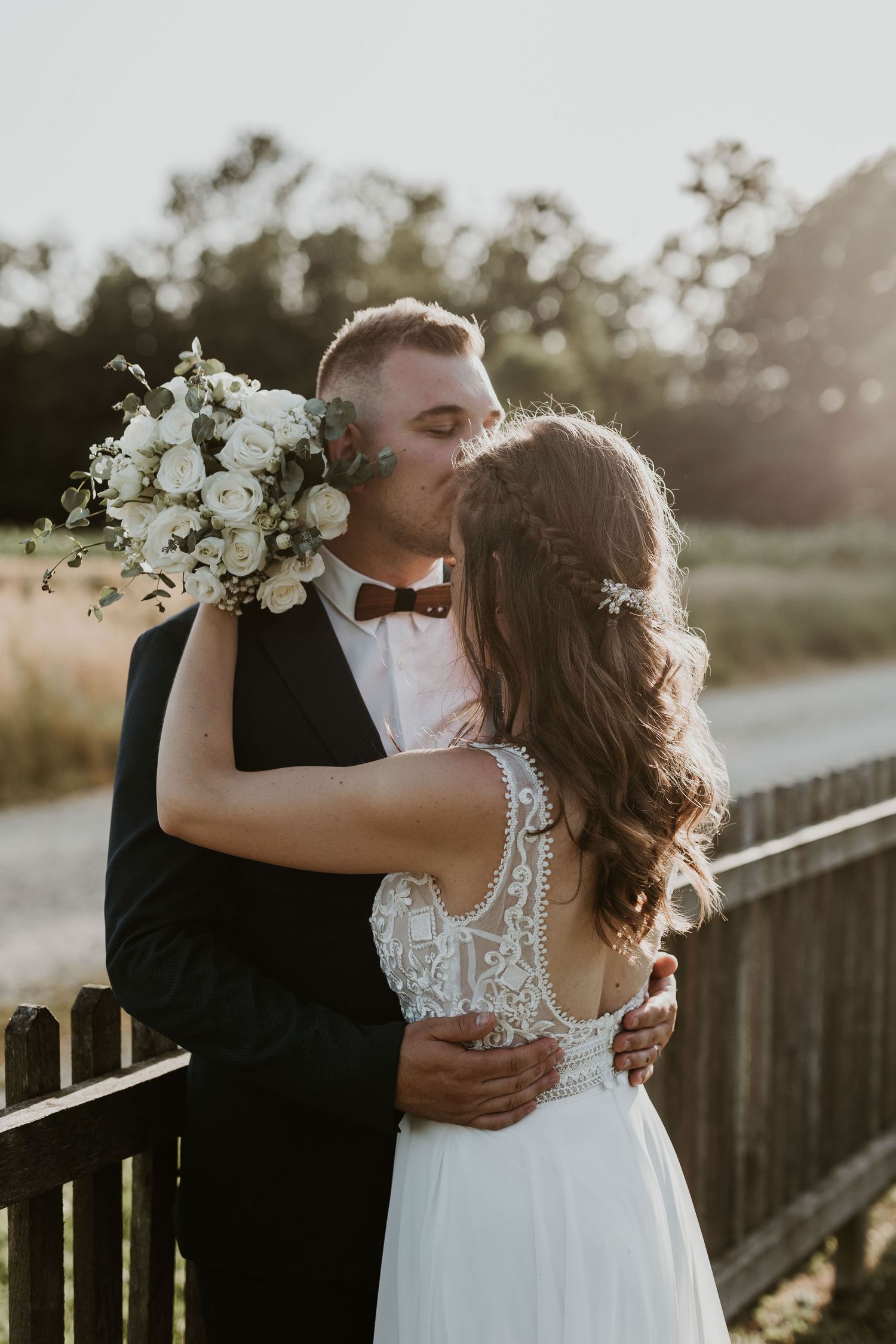 Bride and groom share a passionate kiss at golden hour, bride holding a white floral bouquet.