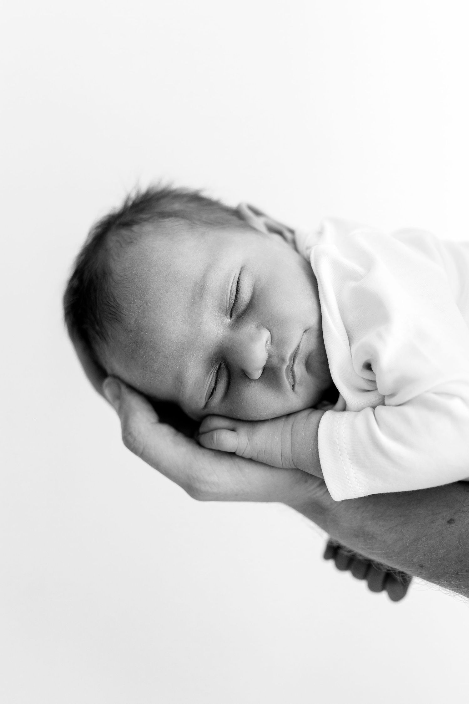 Black and white photo of a sleeping newborn baby cradled gently in an adults hands.