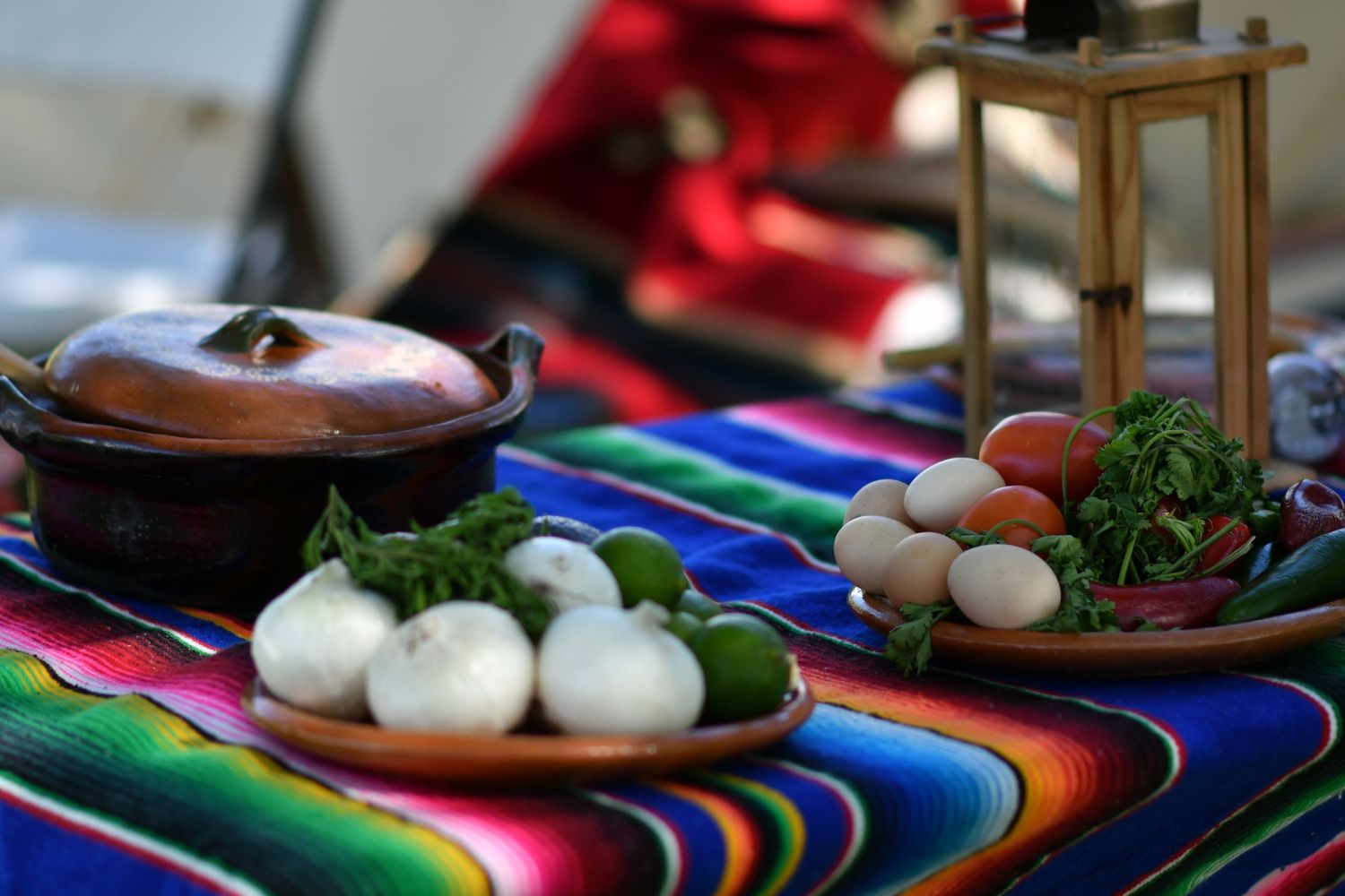 Fresh ingredients displayed on a vibrant Mexican serape with clay cookware and herbs.