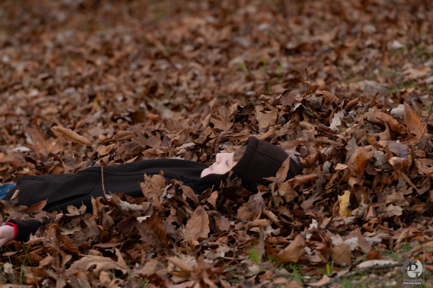 A young boy laying in the leaves enjoying a cool fall day.