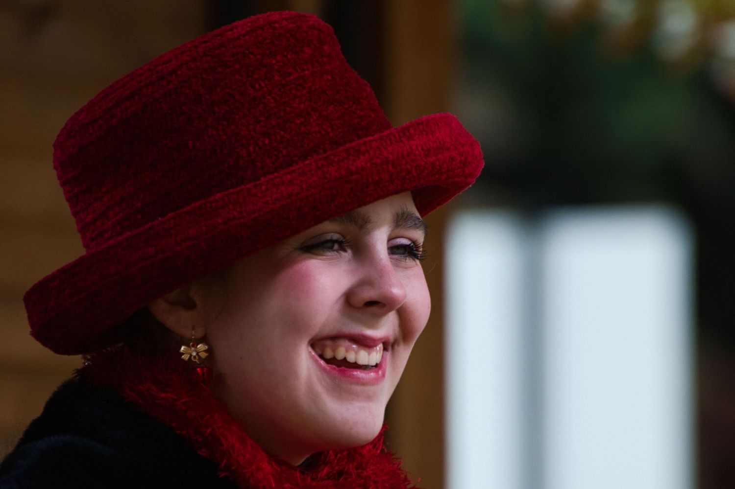 Woman in red hat and black coat smiling against blurred background.