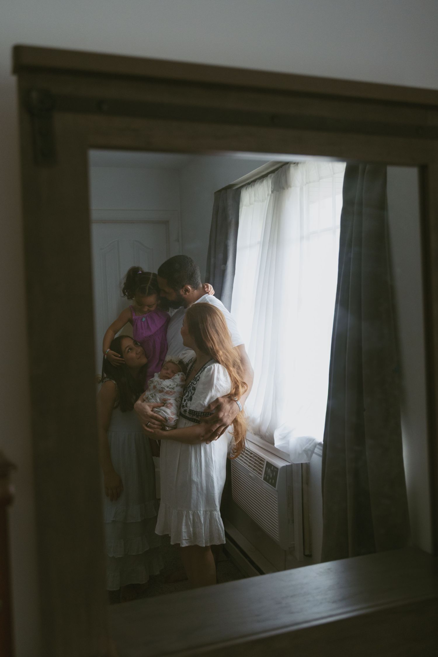 A Family hugging one another, a photo capturing them through the reflection of the mirror during an in-home session in Sussex New Jersey