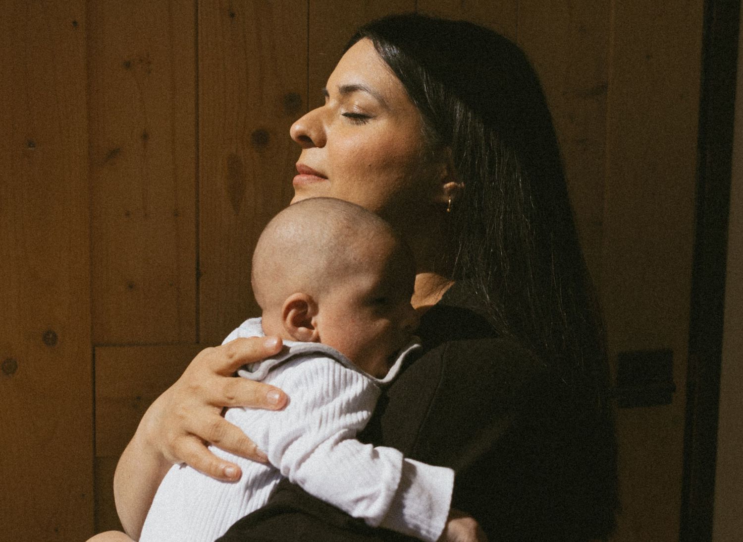 Motherhood photo, of a mother who is embracing her child  on her chest in the window light, being in the moment, in Sussex, New Jersey.