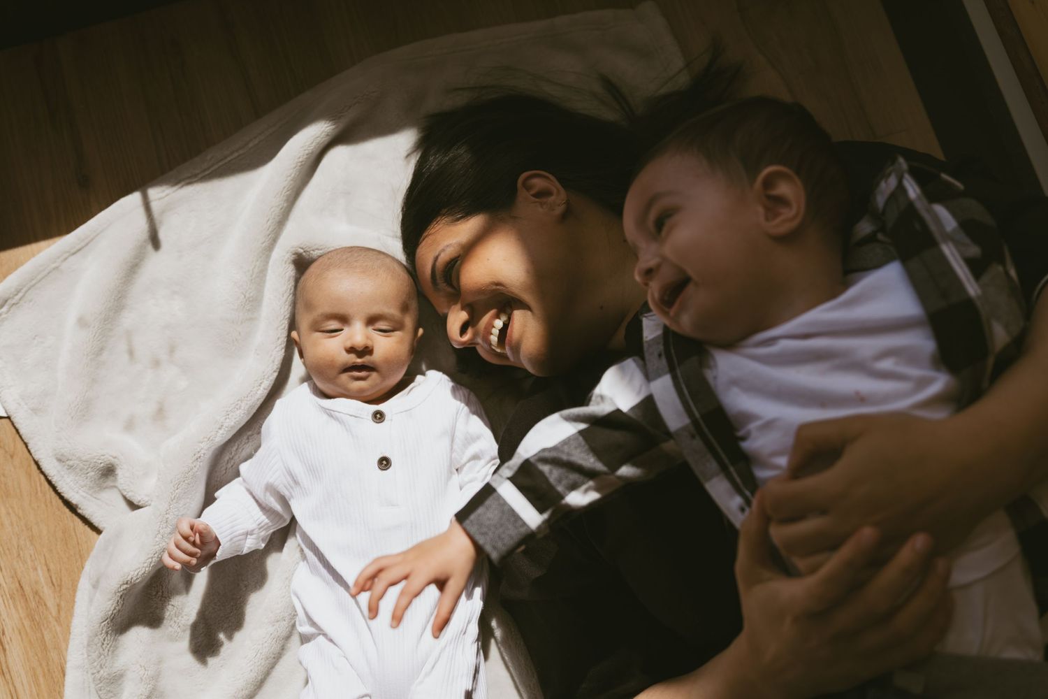 NJ Family lifestyle photoshoot. Mom plays with her children on the floor. Indoor shoot with the sun shining through the windows.