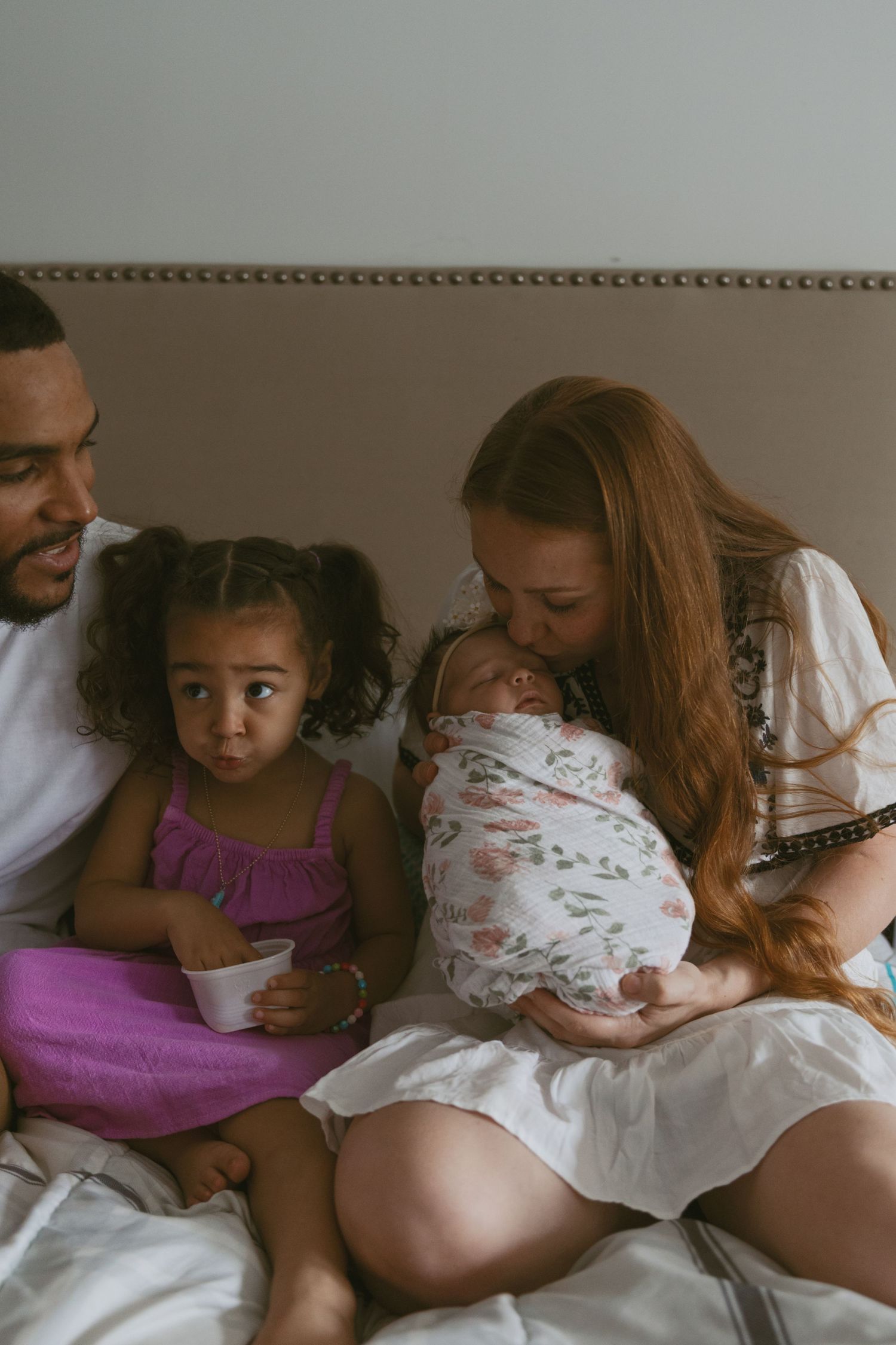 Mother kissing her newborn baby on bed with her family during an a in-home photoshoot in Sussex New Jersey