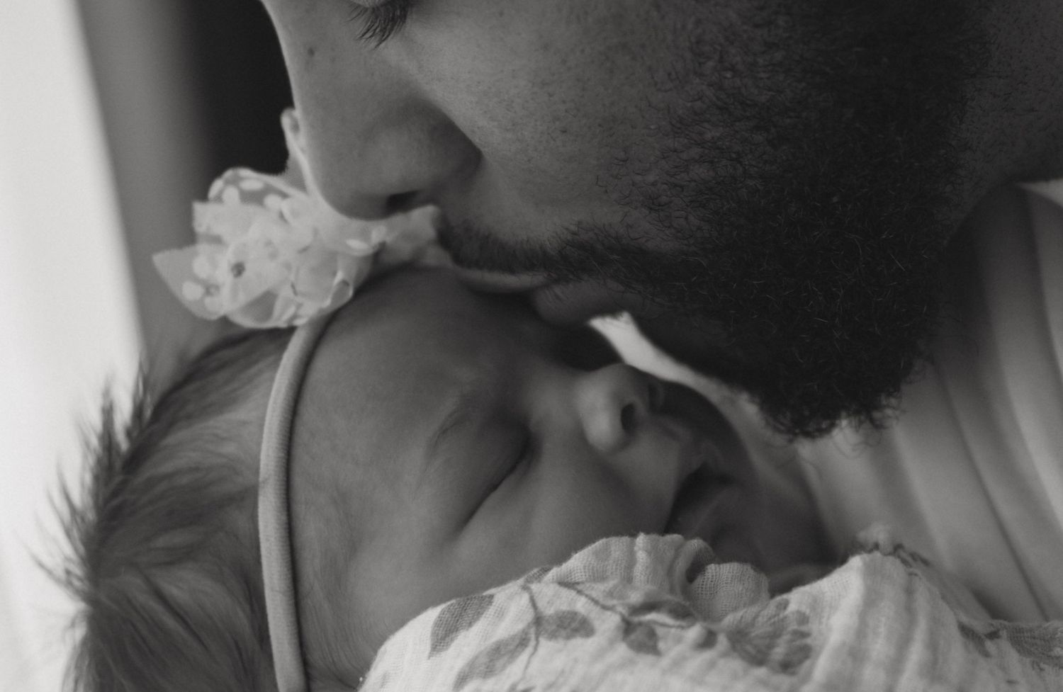 A slow and intentional candid moment of dad kissing his newborn baby on the head during an in-home photoshoot in Sussex New Jersey