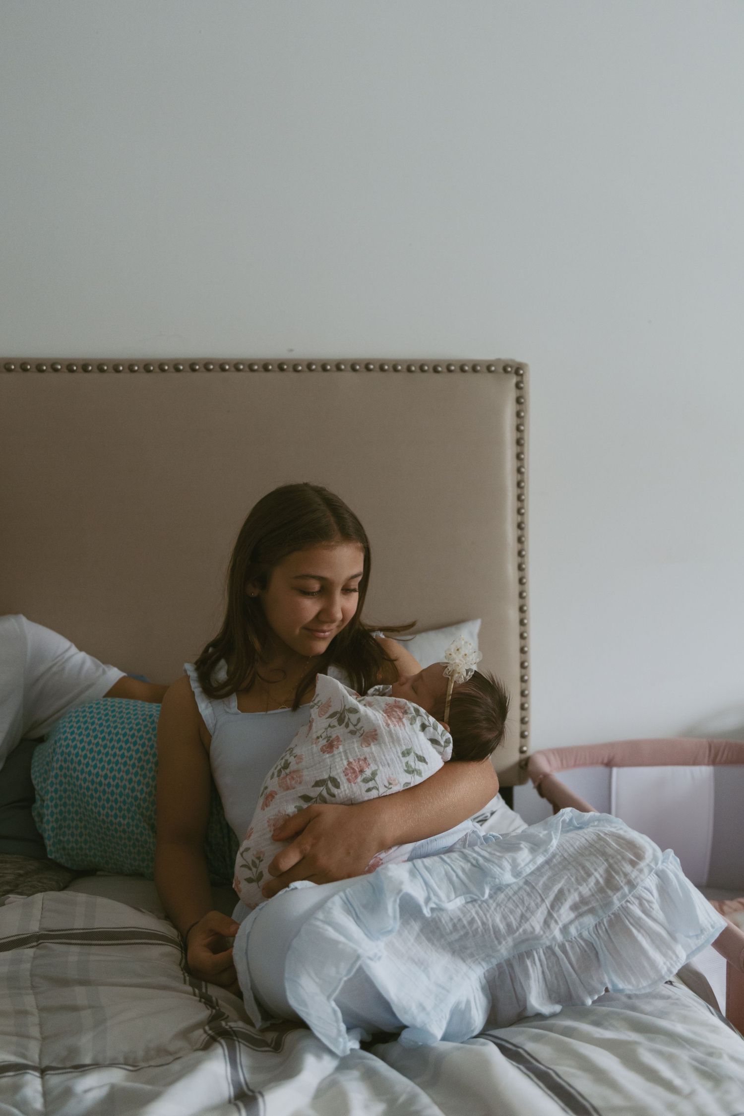 Daughter snuggling and her newborn sister on a bed, during an in-home photoshoot in Sussex County New Jersey.