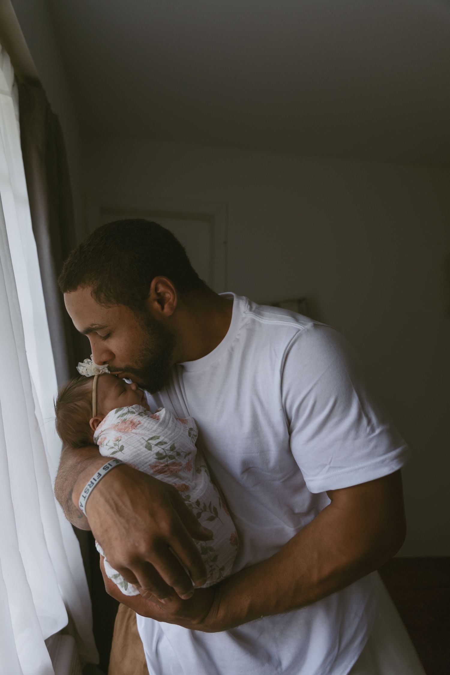 Dad caring for his newborn baby next to the window light during an in-home photoshoot in Sussex County New Jersey