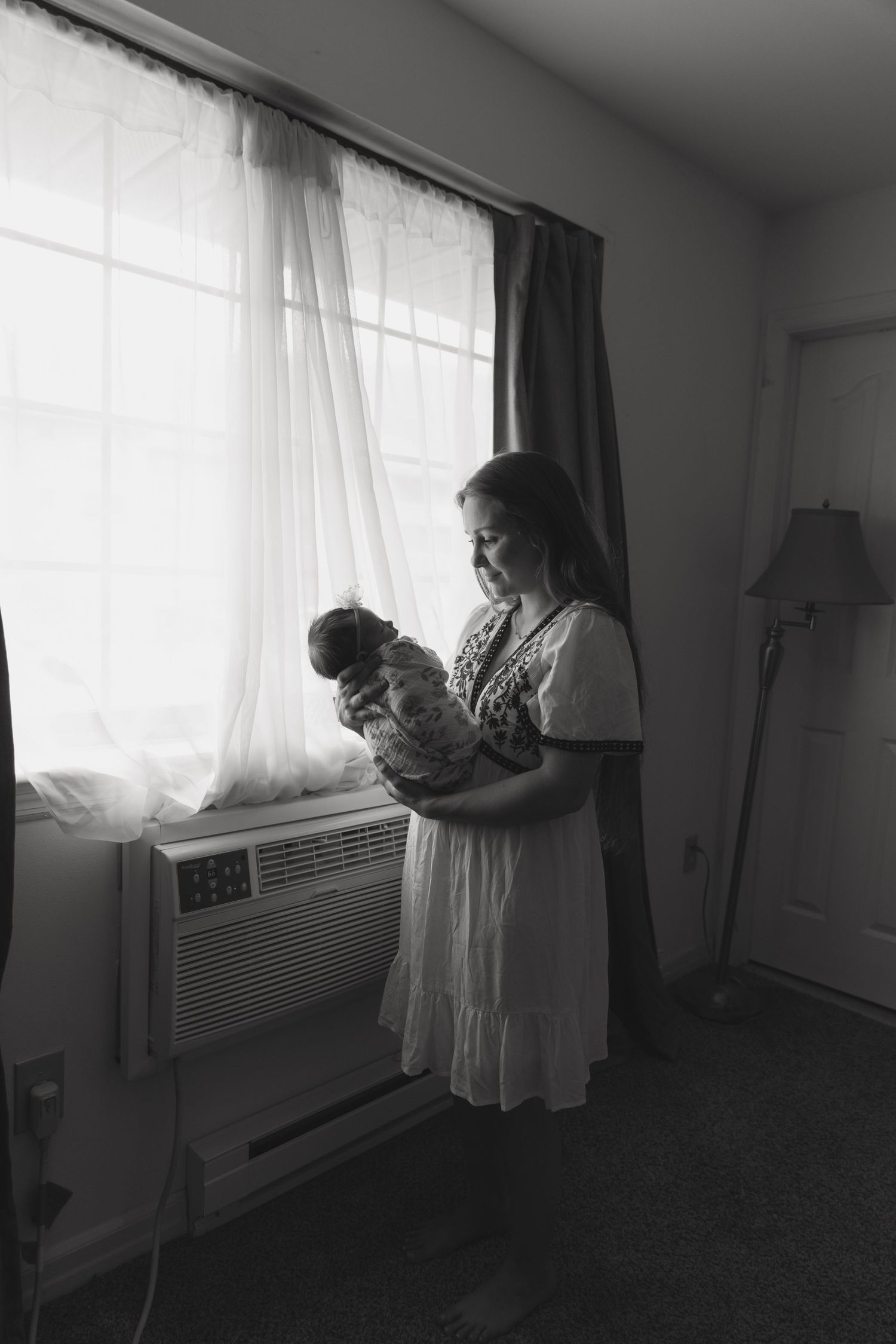 A photo capturing motherhood. A mom looking at her newborn as she cradles the baby near a window at home, in Sussex County New Jersey