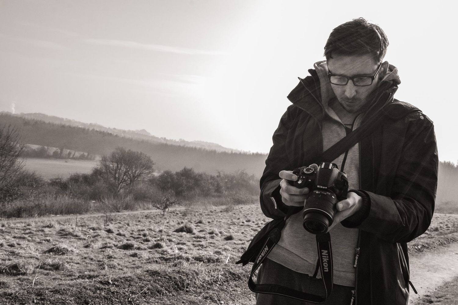 black and white photo of curtis jc photography looking at his camera in sunset lighting