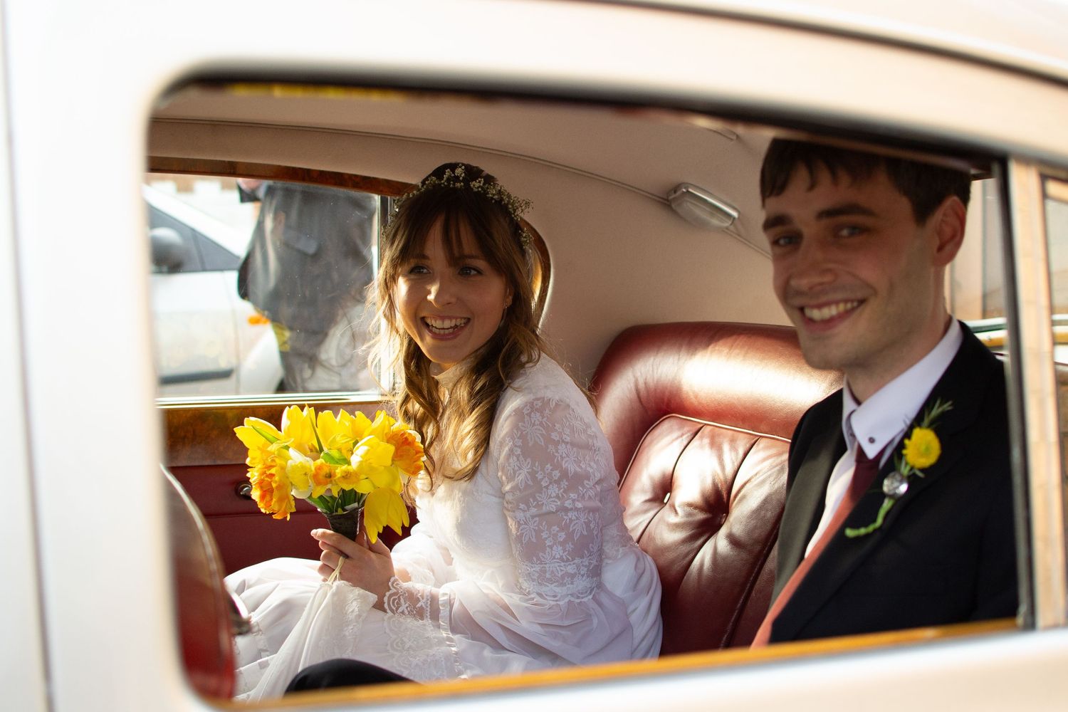 newly wed couple smiling in their hired car, on the way to the reception, bride holding her bouquet