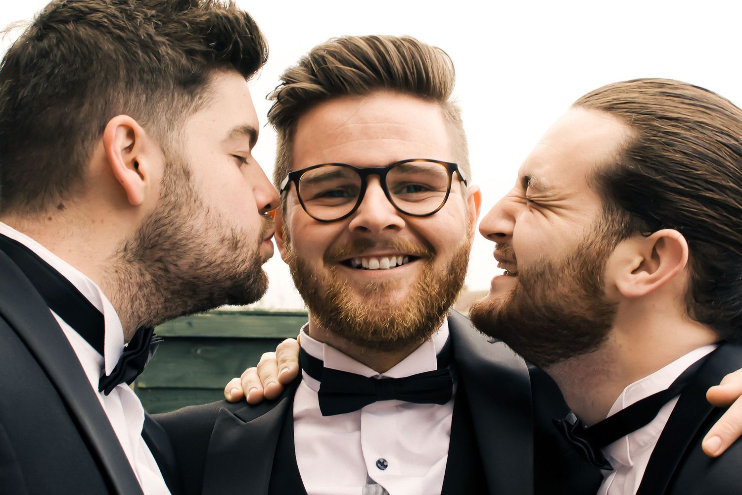 two groomsman kissing the groom who is smiling before his wedding