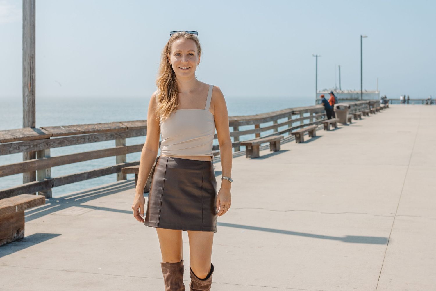 A person walks along a sunny oceanfront pier wearing athletic clothing and carrying a water bottle in Huntington Beach.